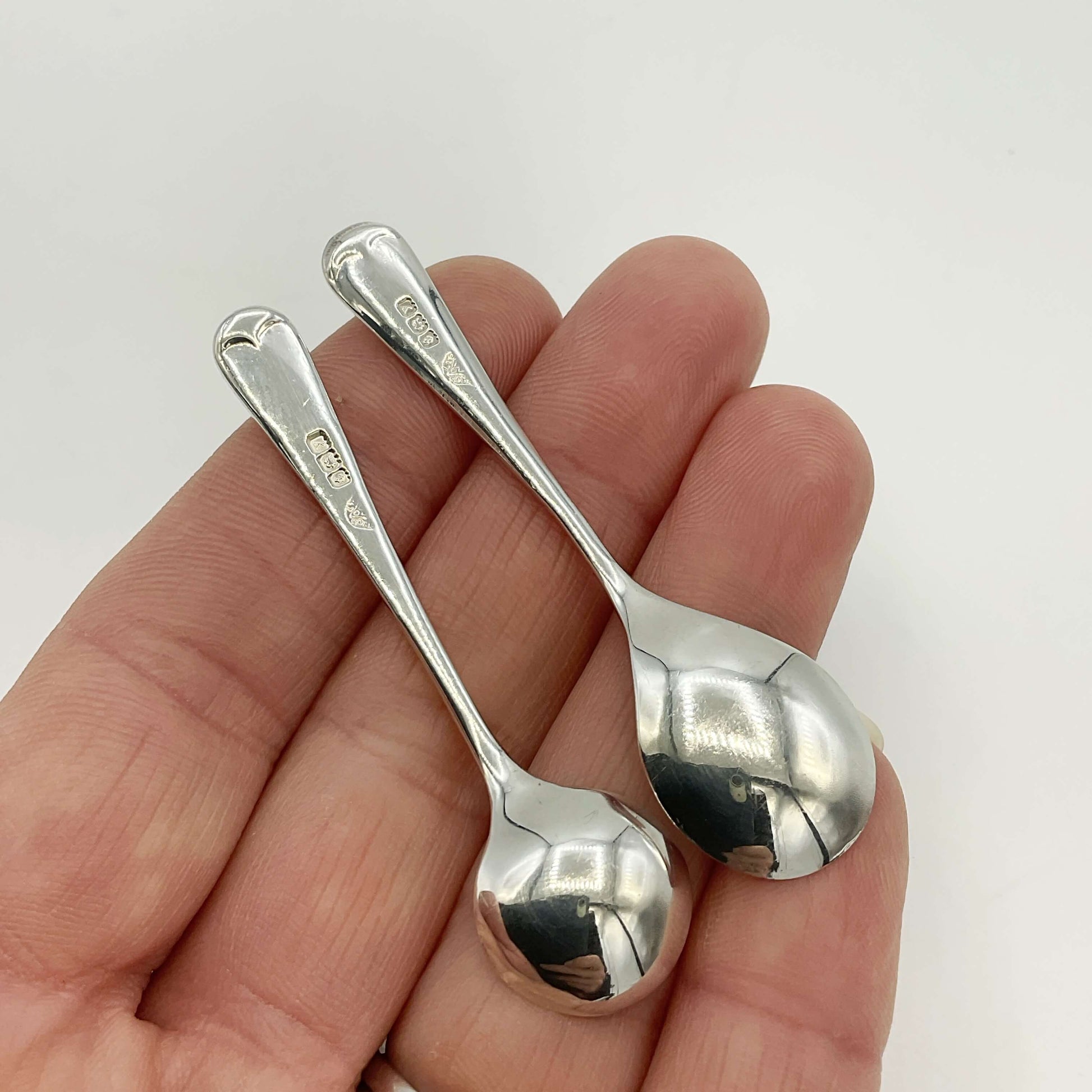 Two silver spoons held in a hand against a white background