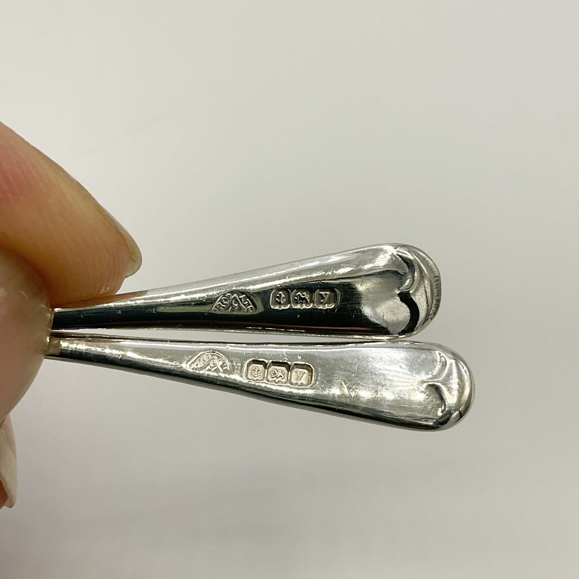 Two silver spoons with hallmarks in a hand against a white background