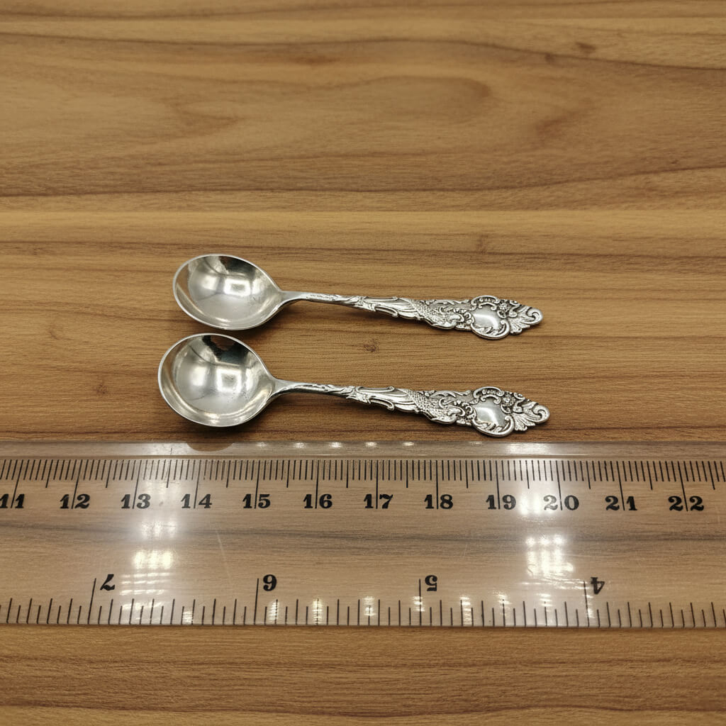 Two silver spoons on a wooden surface with a ruler for scale.