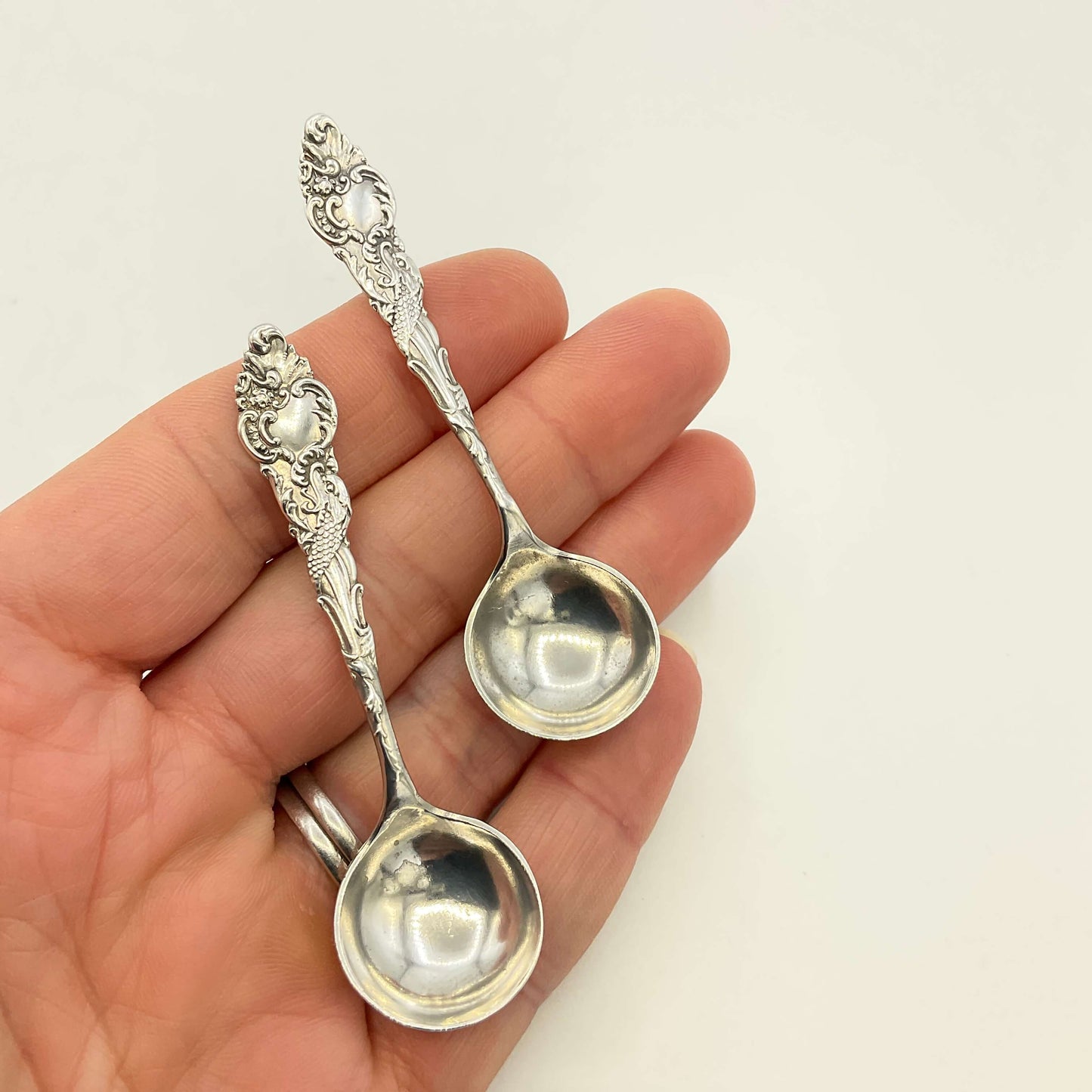 Two silver spoons held in a hand against a plain background