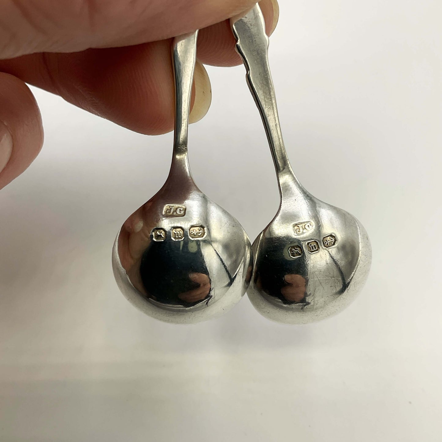 Two silver spoons showing hallmarks held by a hand against a white background