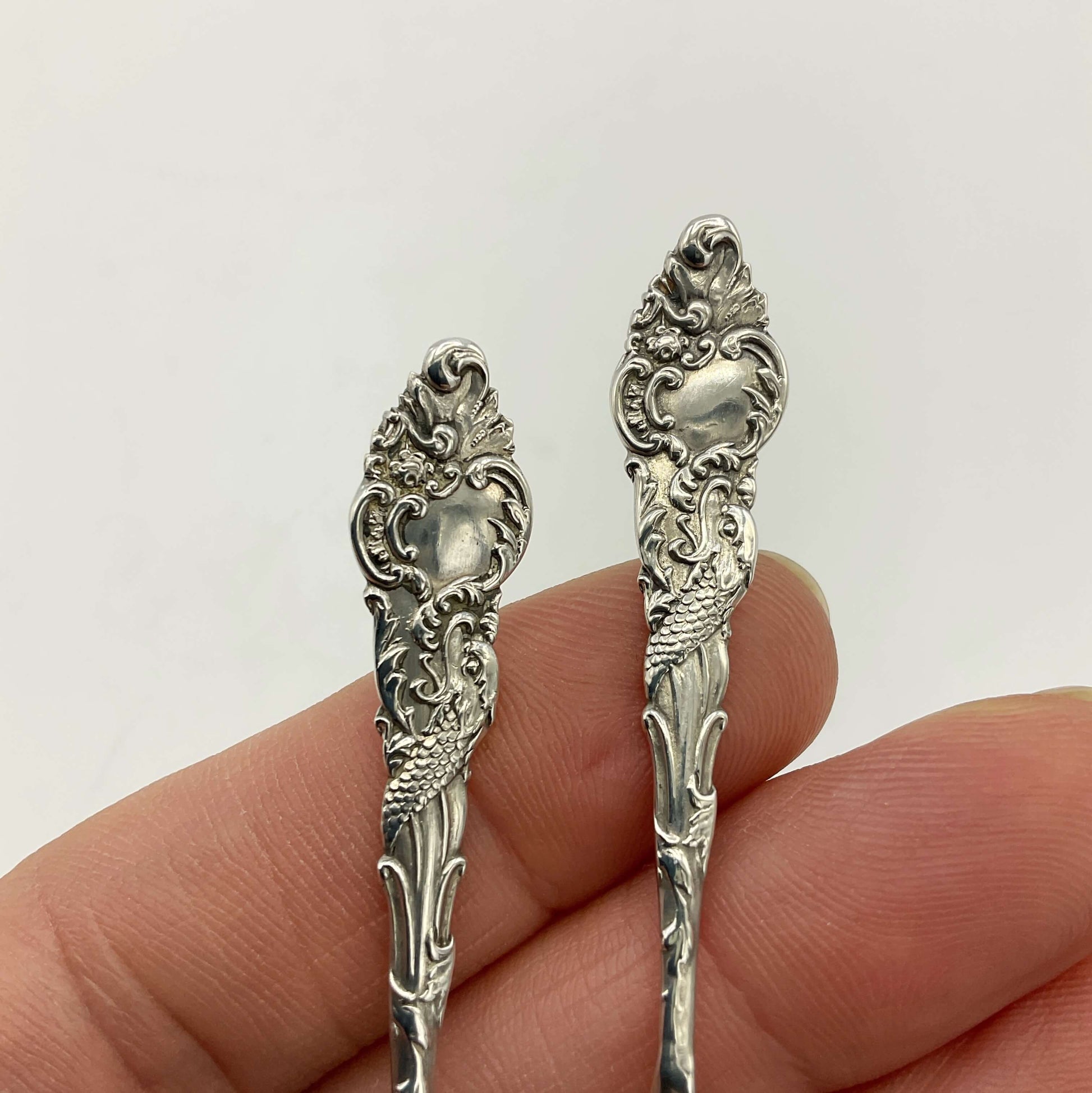 Two ornate silver spoons held between fingers against a white background