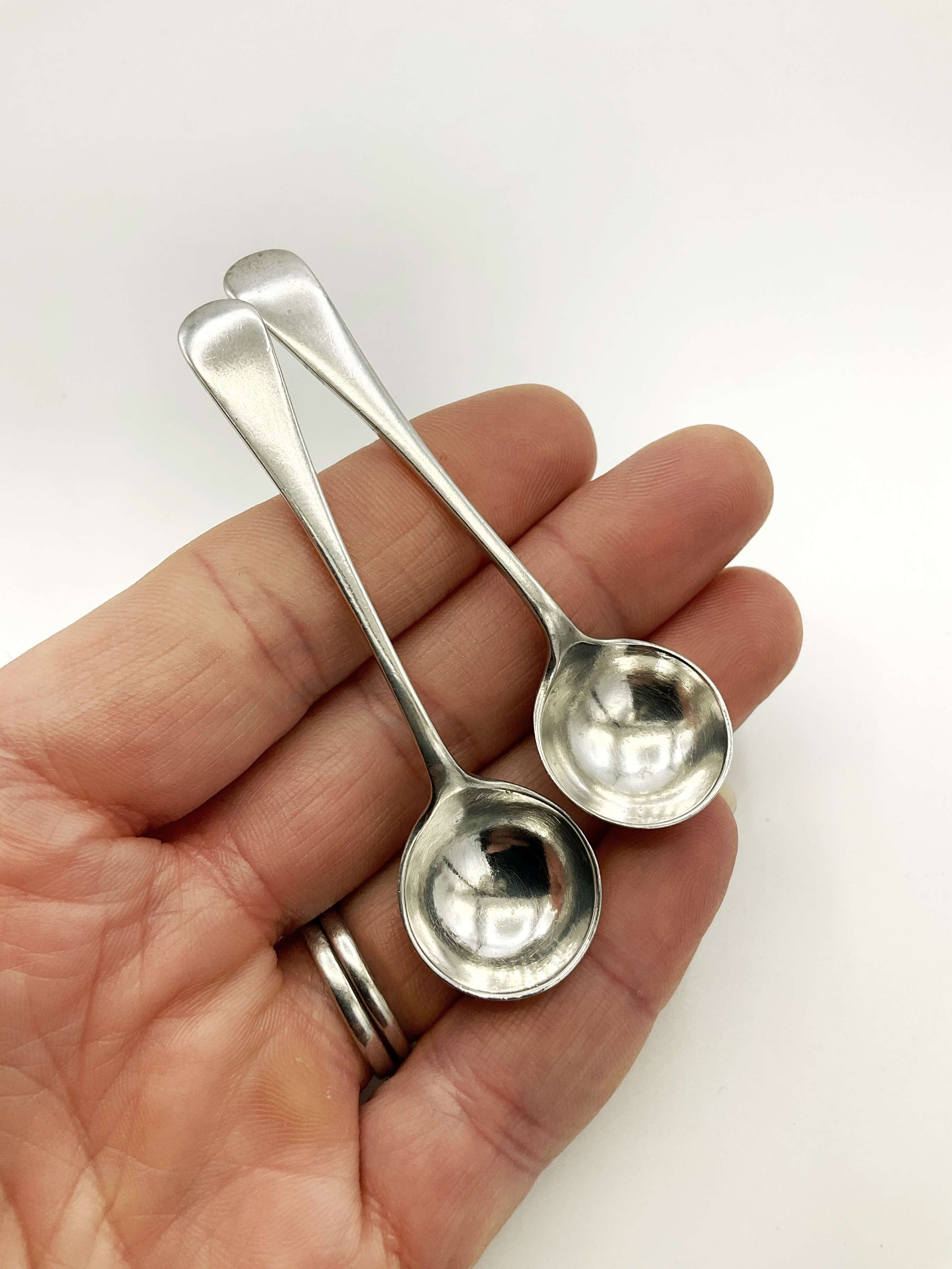Two small silver spoons held in a hand against a white background