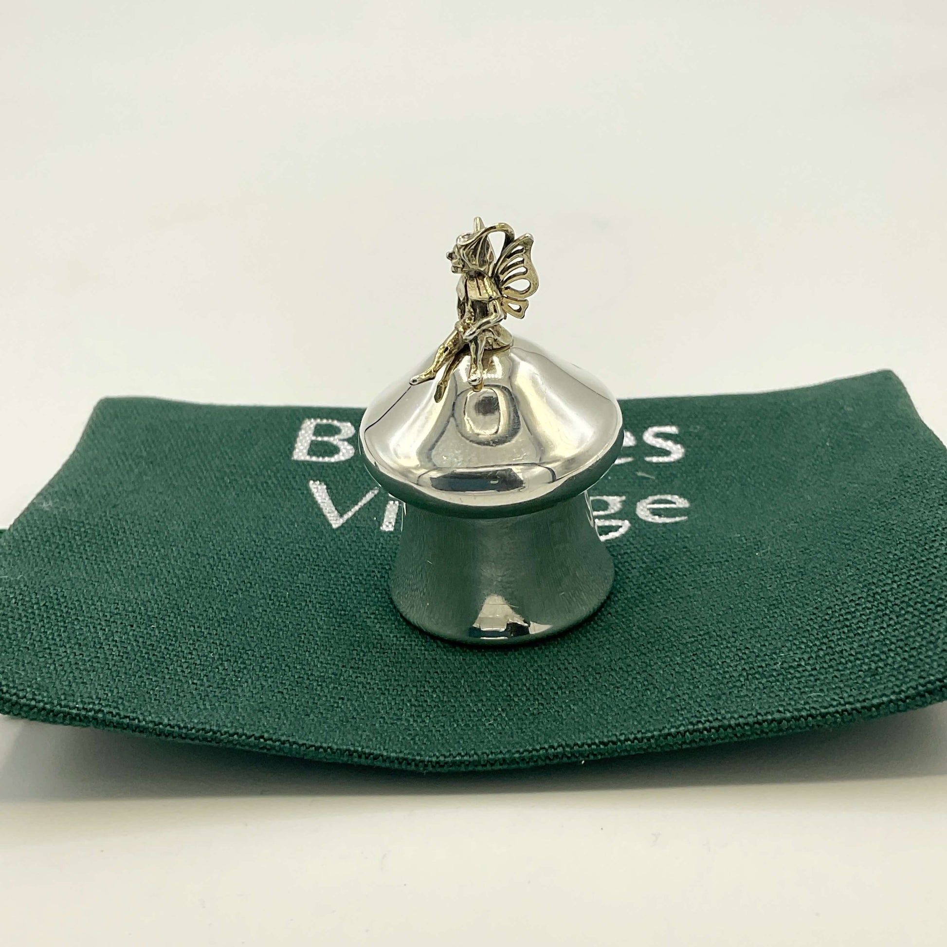 Silver pill box with a fairy on top on a green gift bag and white background.