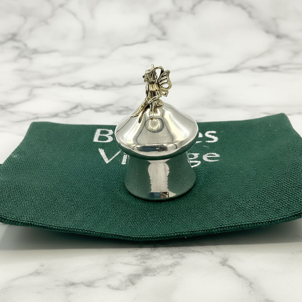 silver pill box with fairy on top on green bag on marble