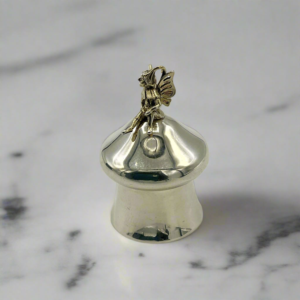 Silver pill box with a gold fairy on top on a marble background