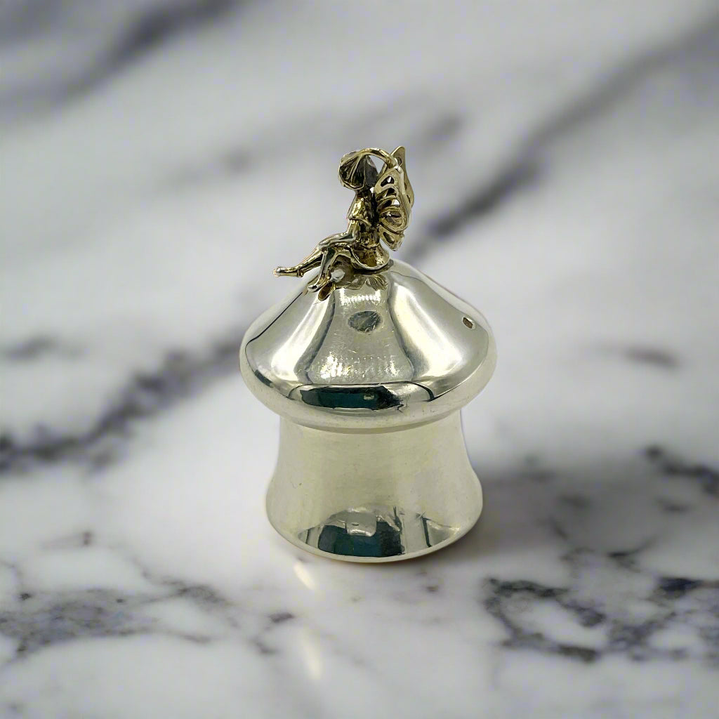Silver pill box with a gold fairy charm on a marble background 