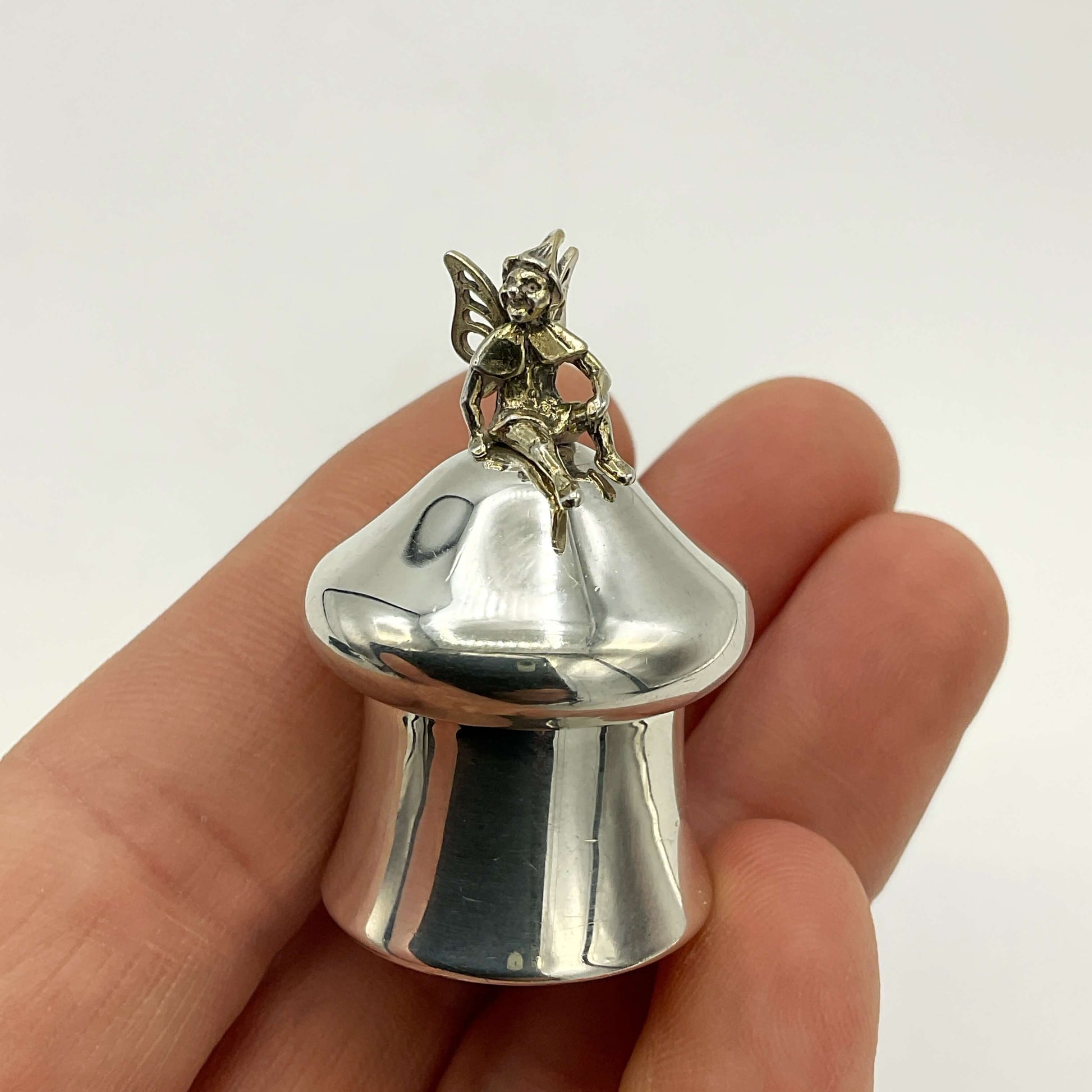 Silver pill box with fairy figure held in a hand against a white background