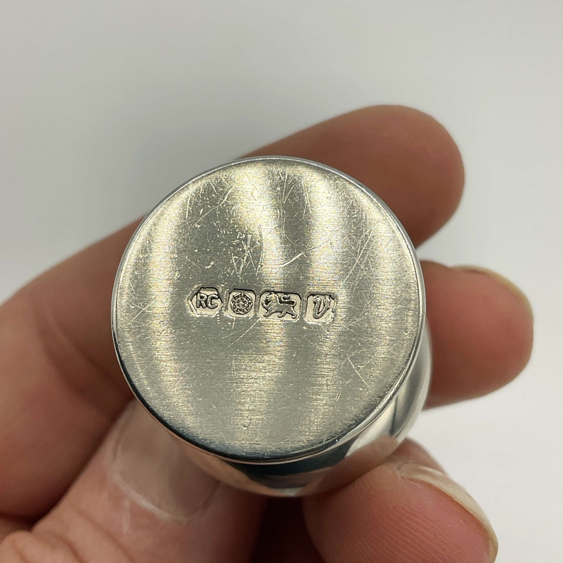 Silver pill box base held between fingers with visible hallmark on a white background