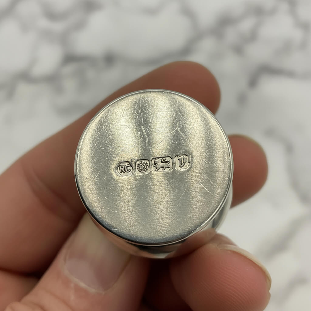 Silver pill box with hallmarks on base held in a hand with a blurred background