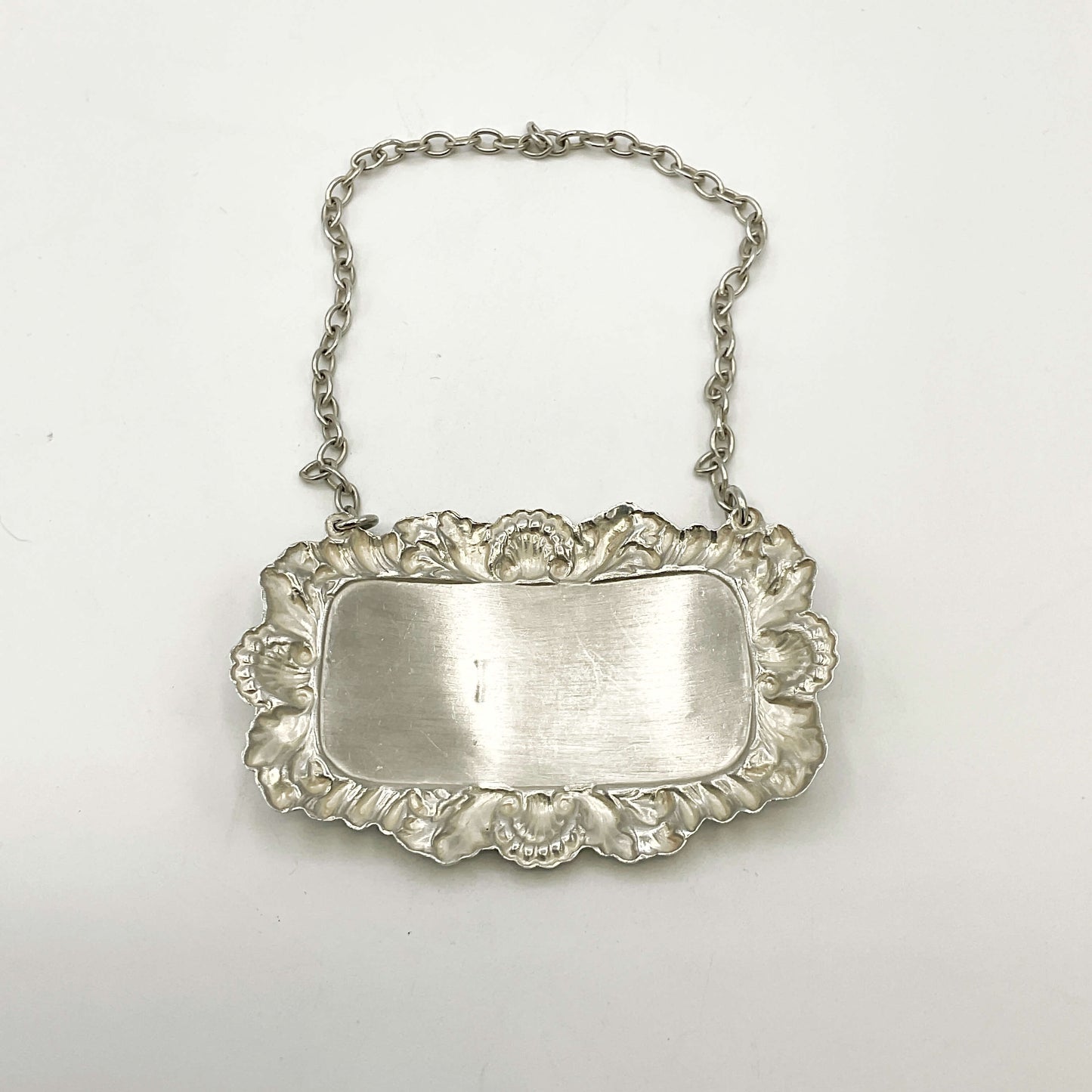 Back of silver decanter label with chain on a white background