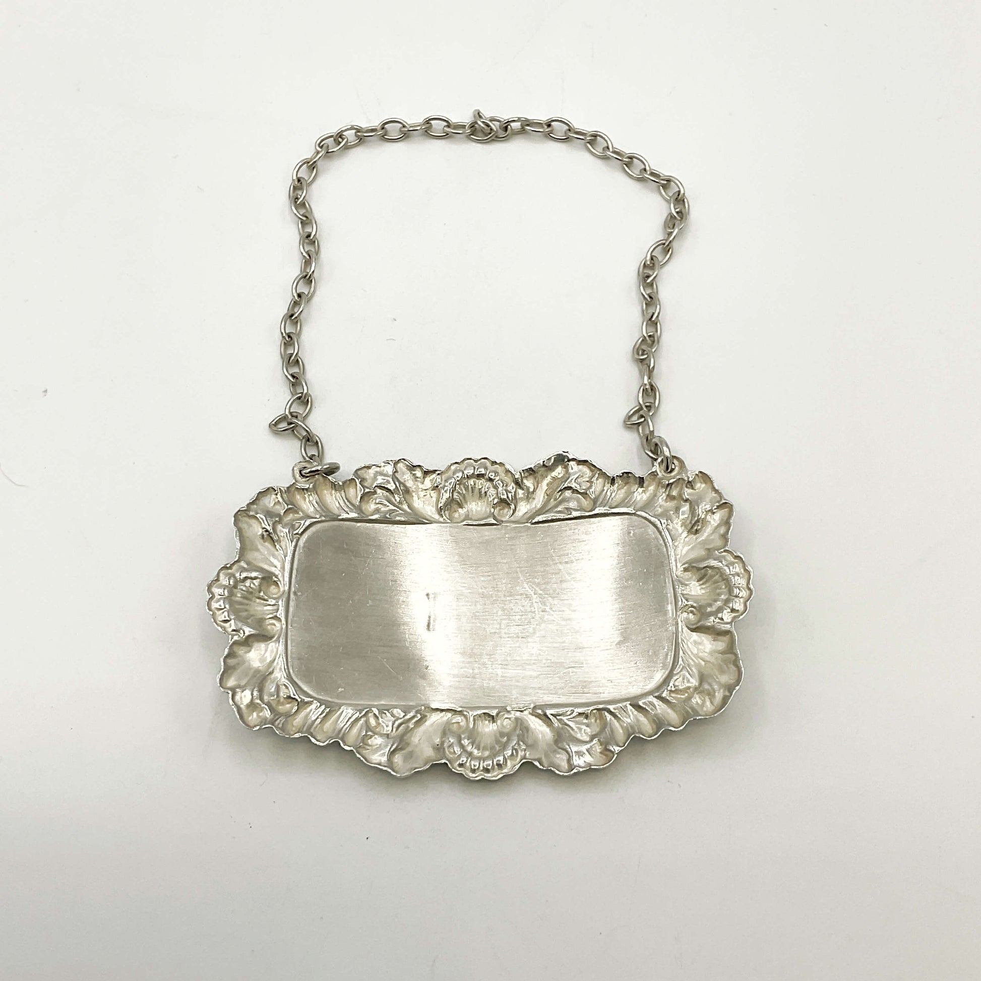 Back of silver decanter label with chain on a white background