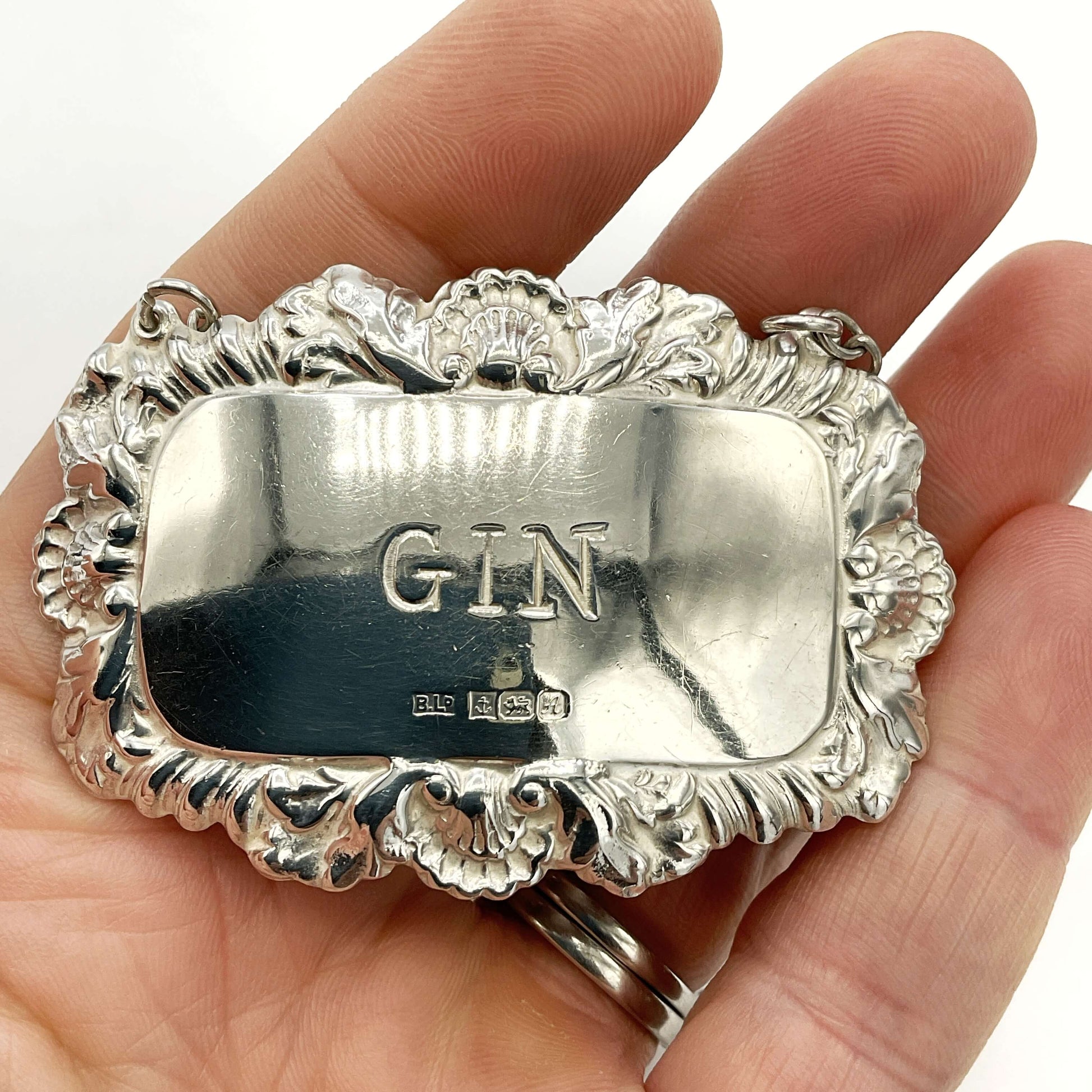 Silver gin label held in a hand against a white background
