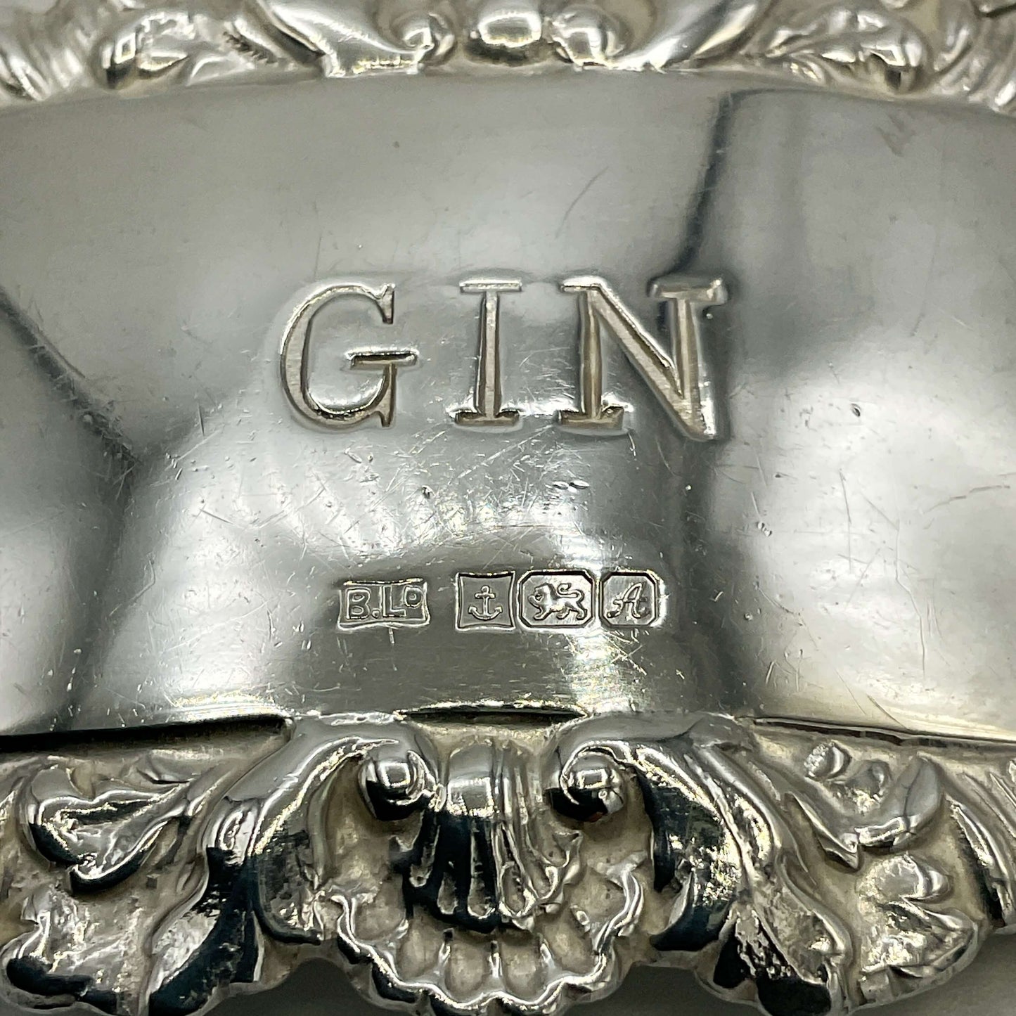 Close-up of a silver gin label with 'GIN' and hallmarks engraved on it.
