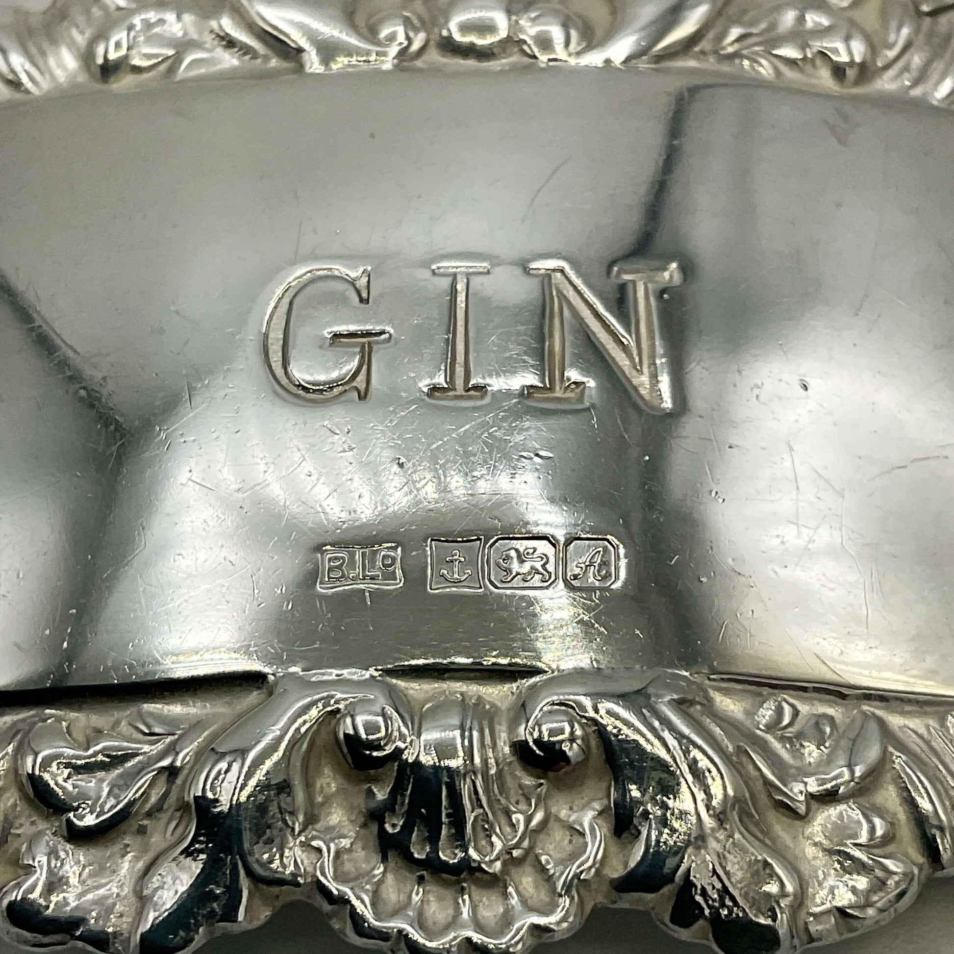 Close-up of a silver gin label with 'GIN' and hallmarks engraved on it.