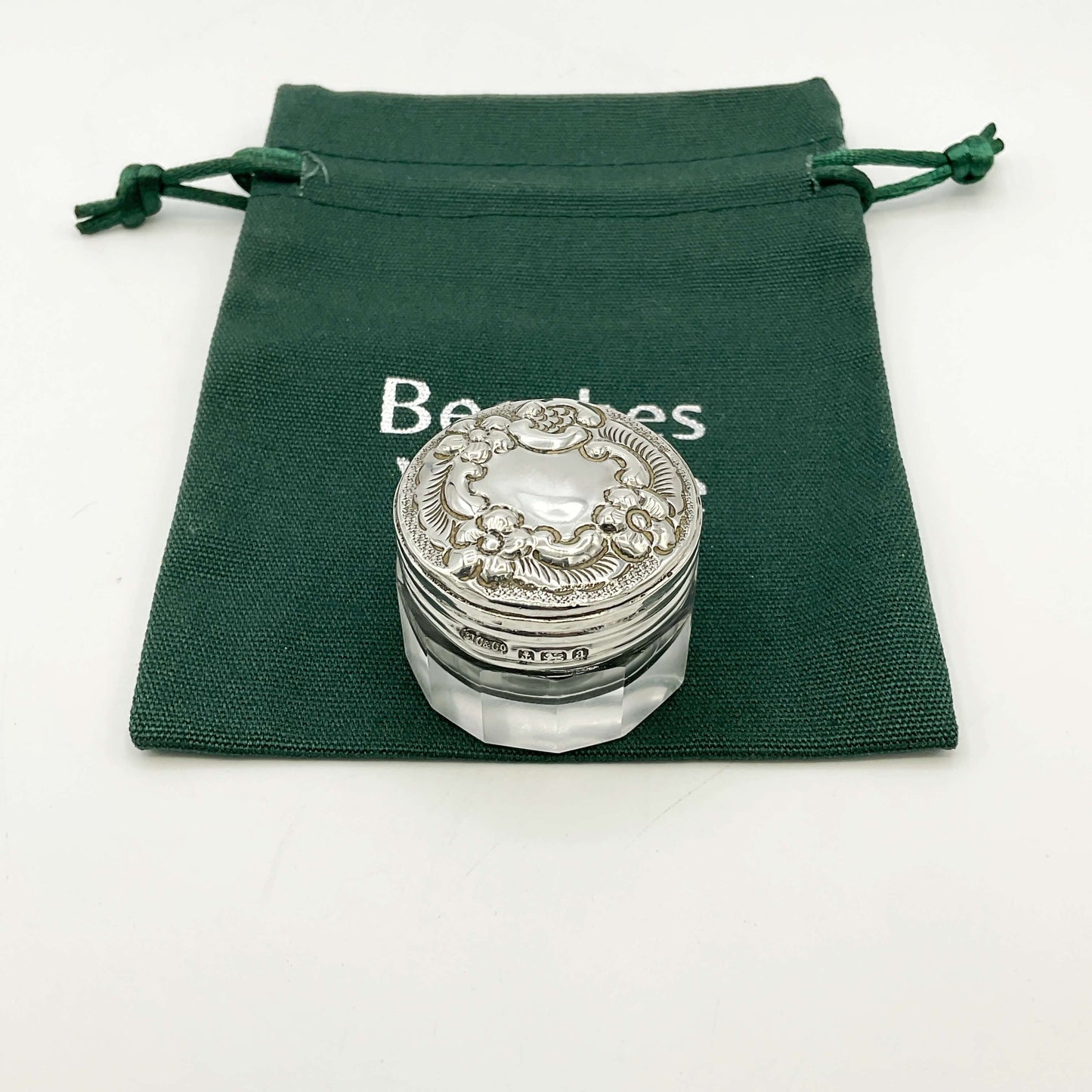 Silver lidded glass jar on a green drawstring bag with a white background .