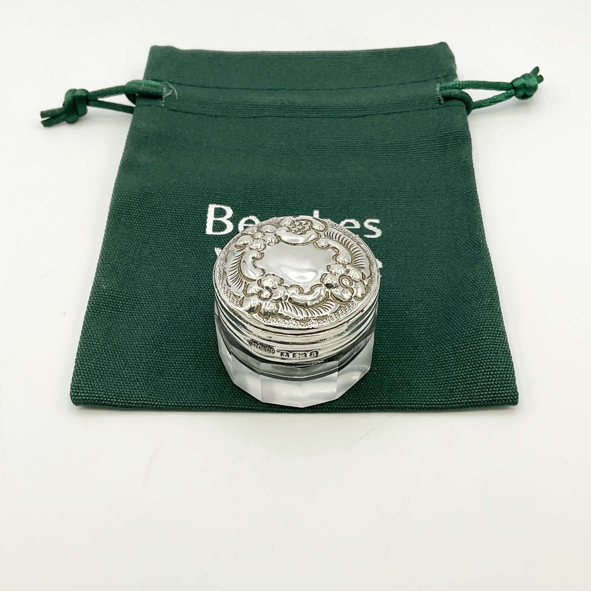 Silver lidded glass jar on a green drawstring bag with a white background .