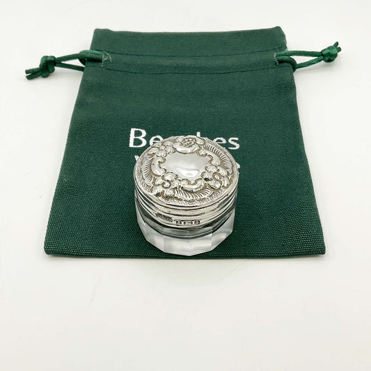Silver lidded glass jar on a green drawstring bag with a white background .