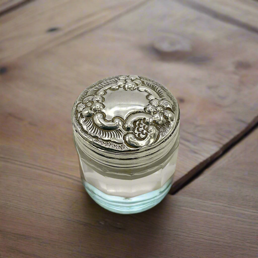 Decorative glass jar with ornate silver lid on a wooden surface