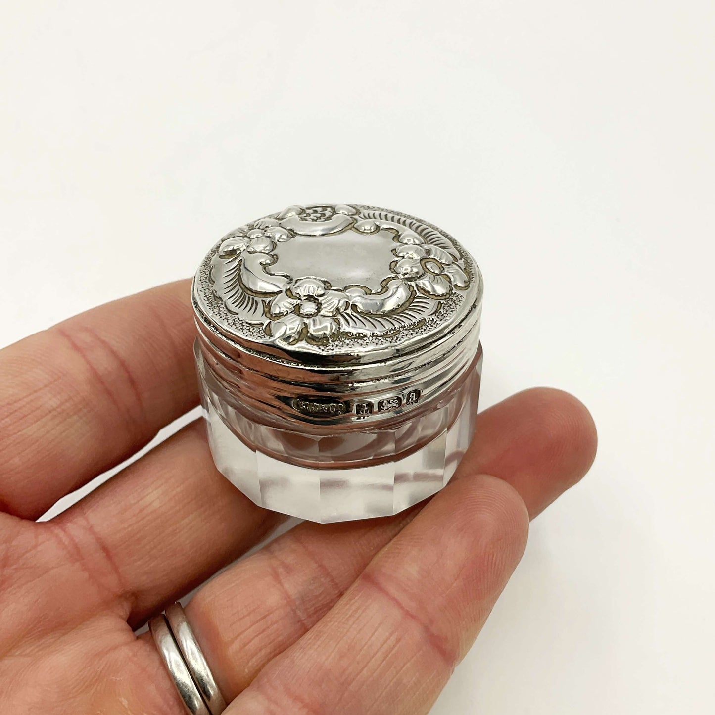 Decorative silver lid on a clear glass container held in a hand against a white background