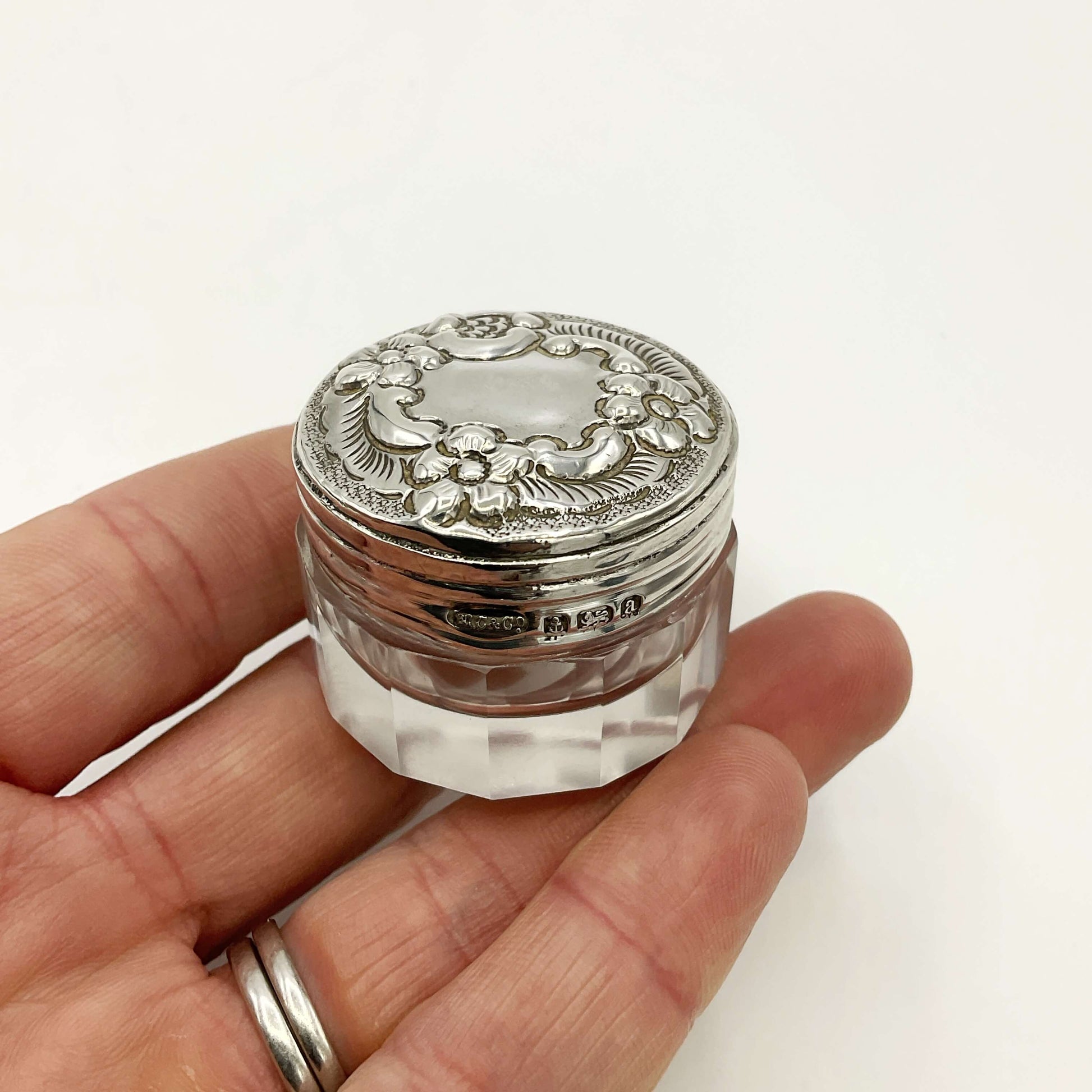 Decorative silver lid on a clear glass container held in a hand against a white background