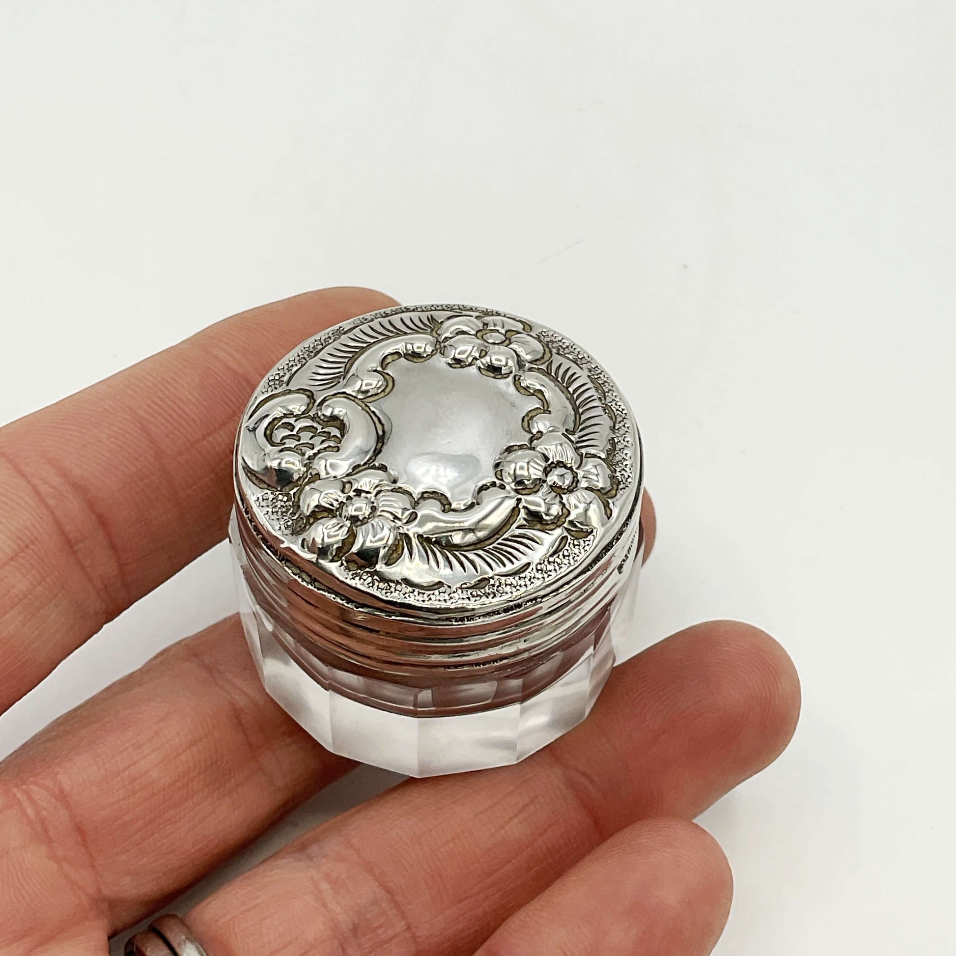 Decorative silver and glass jar  held in a hand against a white background