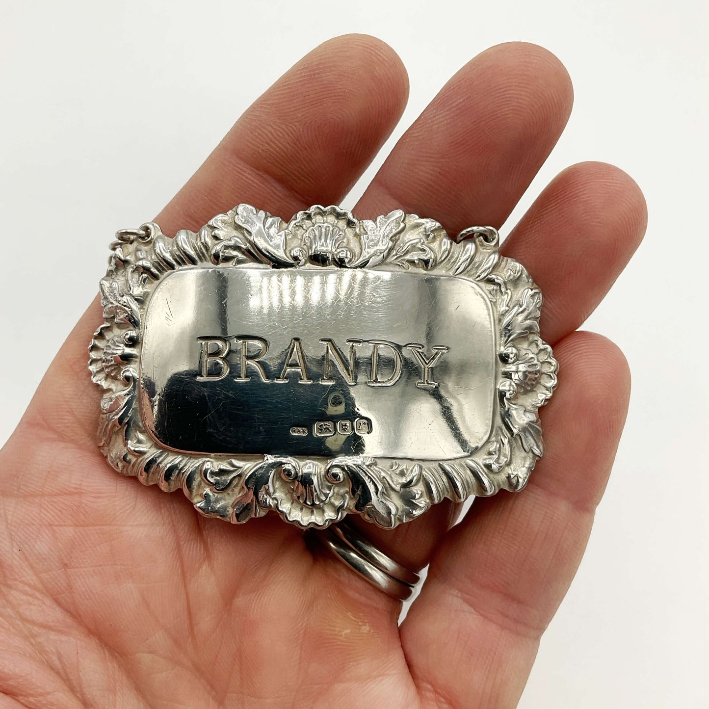 Silver 'BRANDY' label held in a hand against a white background