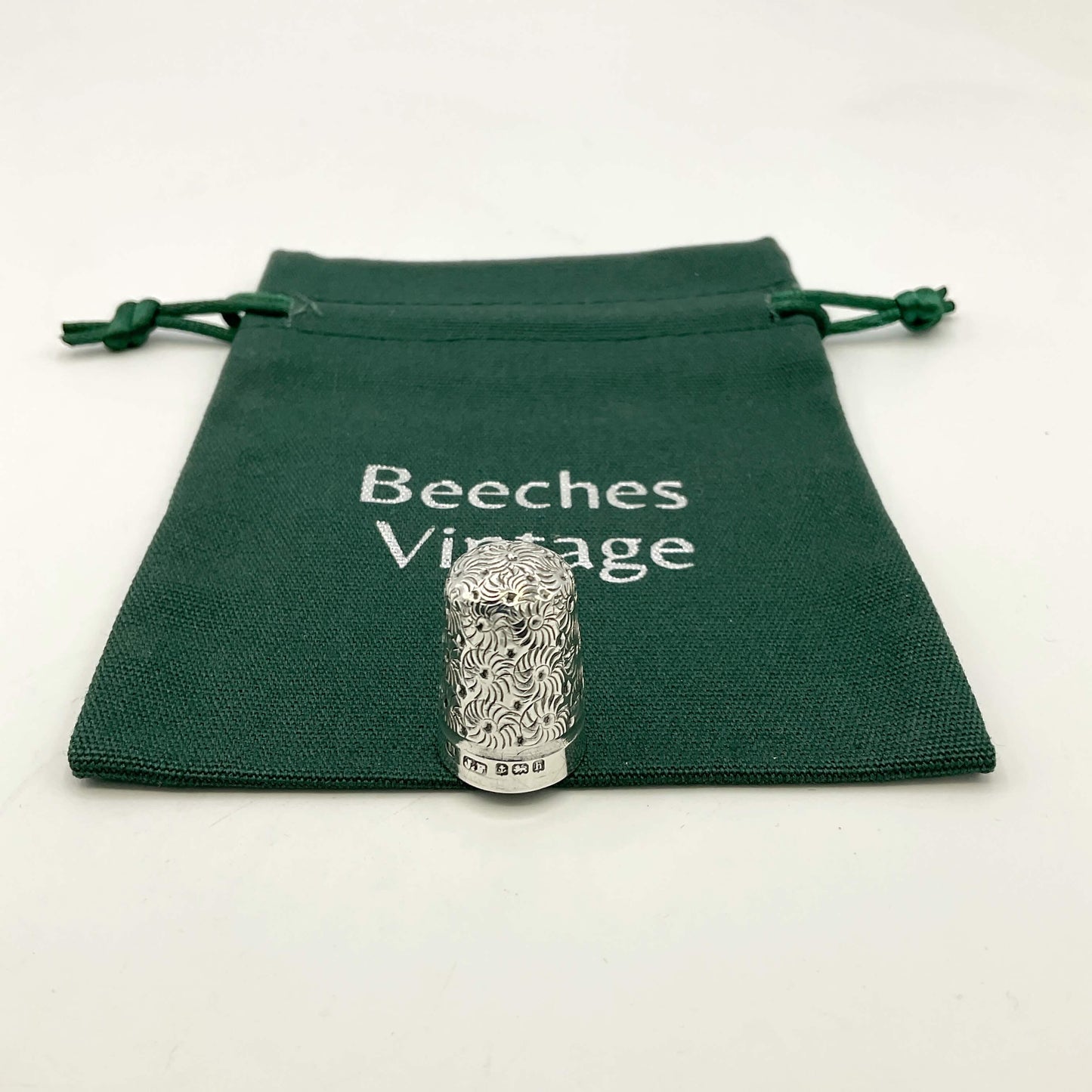 Silver thimble with intricate design on a green 'Beeches Vintage' pouch