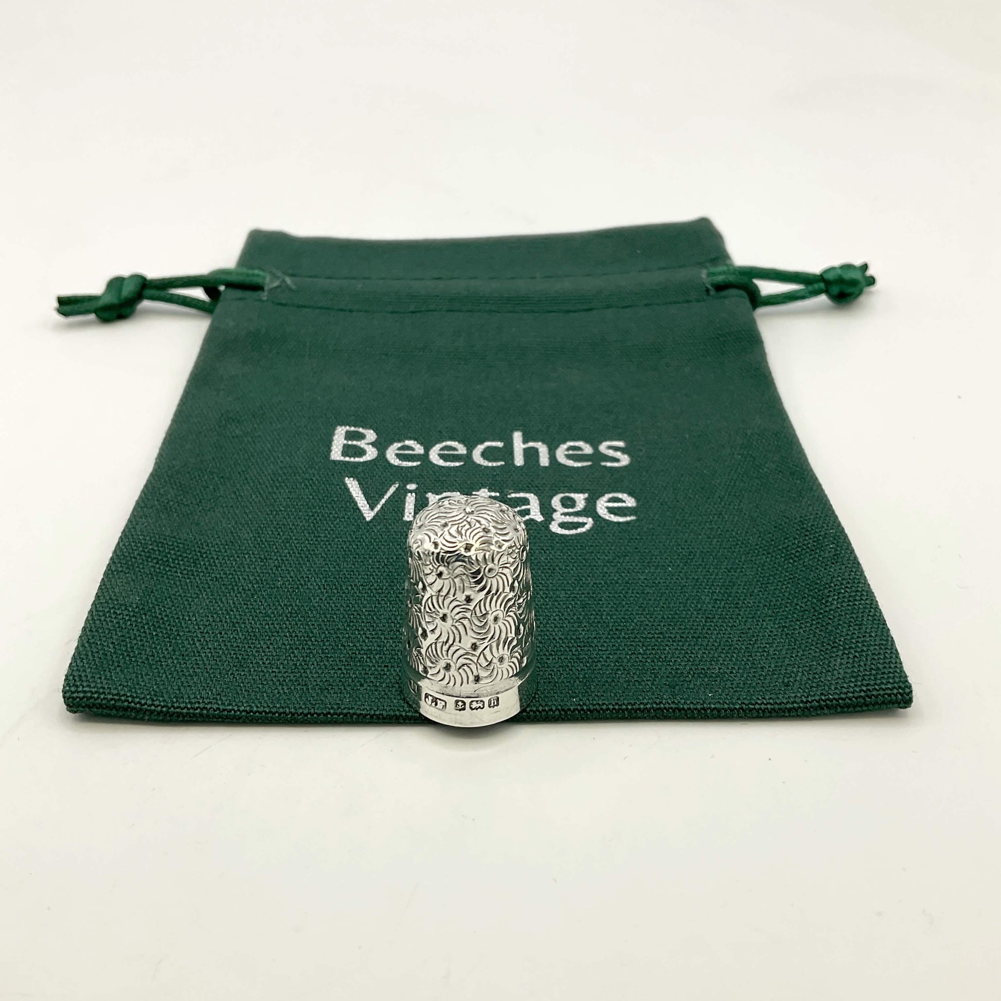 Silver thimble with intricate design on a green 'Beeches Vintage' pouch