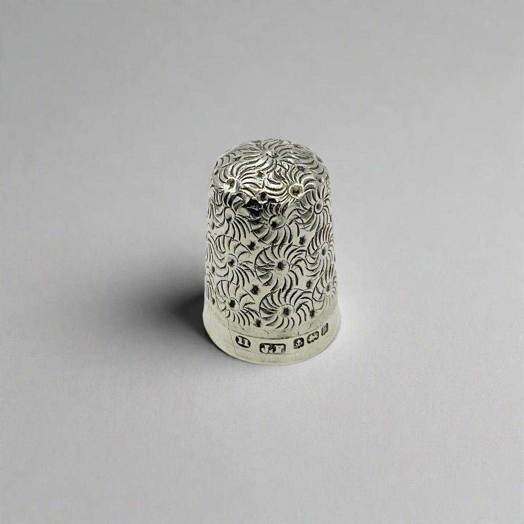 Silver thimble with intricate patterns on a light background