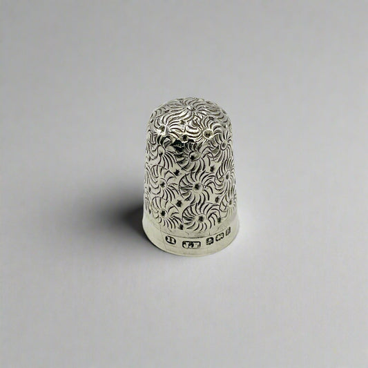 Silver thimble with intricate patterns on a light background