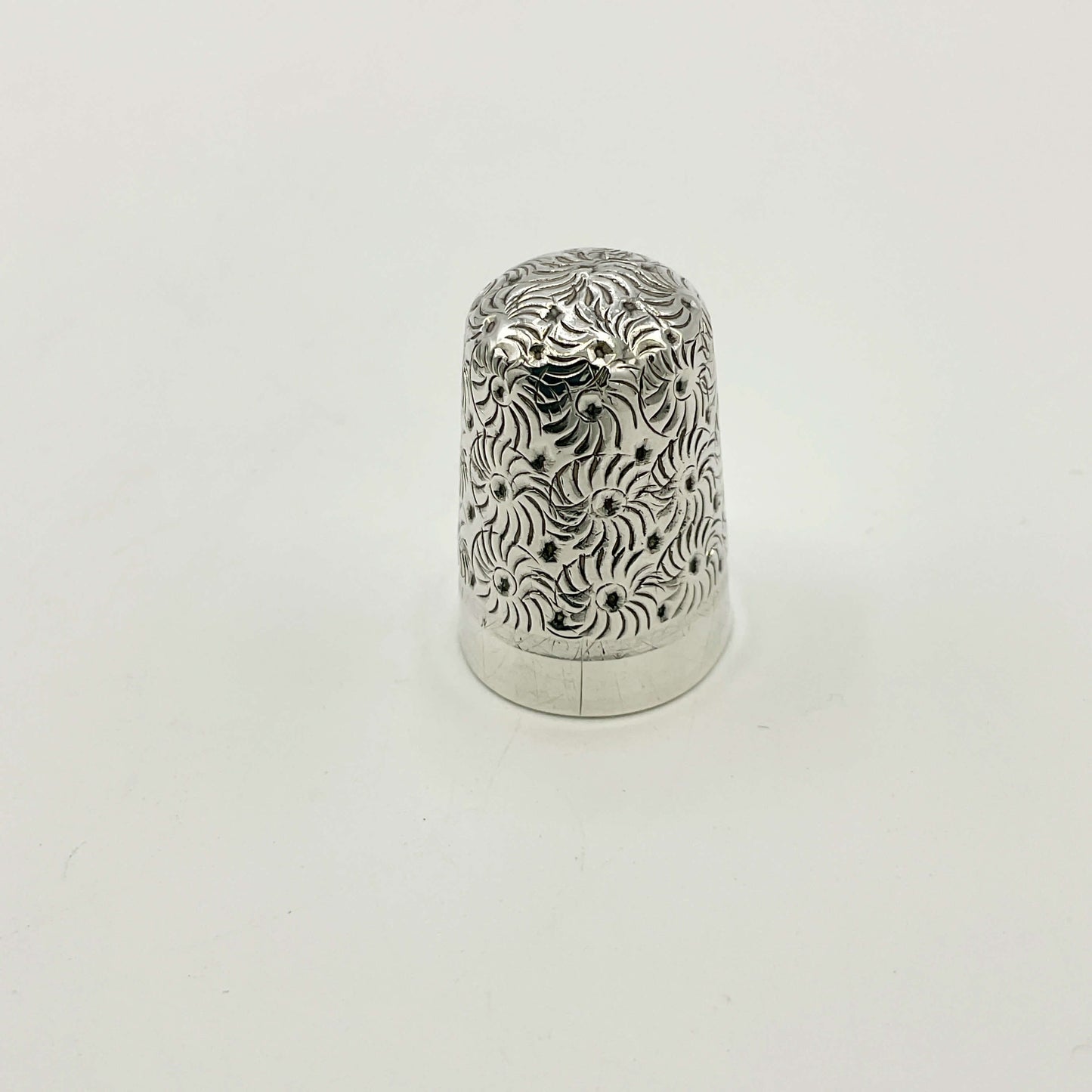 Silver thimble with intricate patterns on a white background