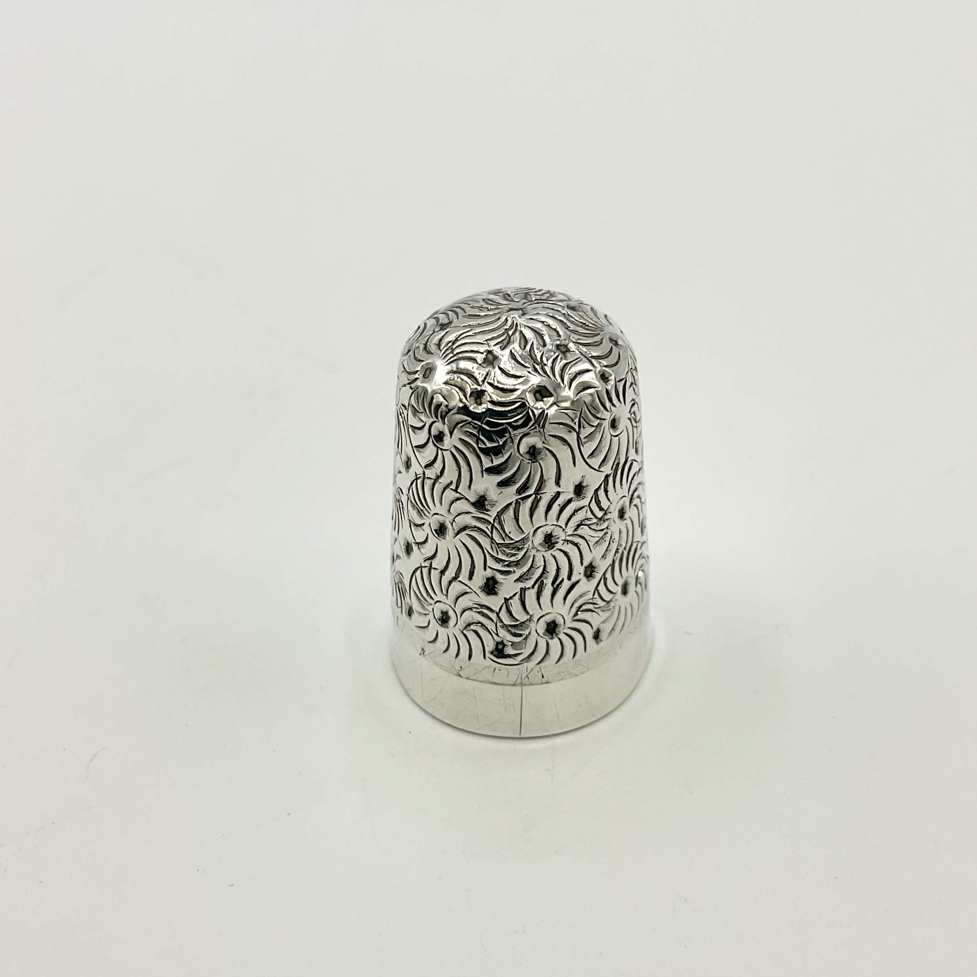 Silver thimble with intricate patterns on a white background