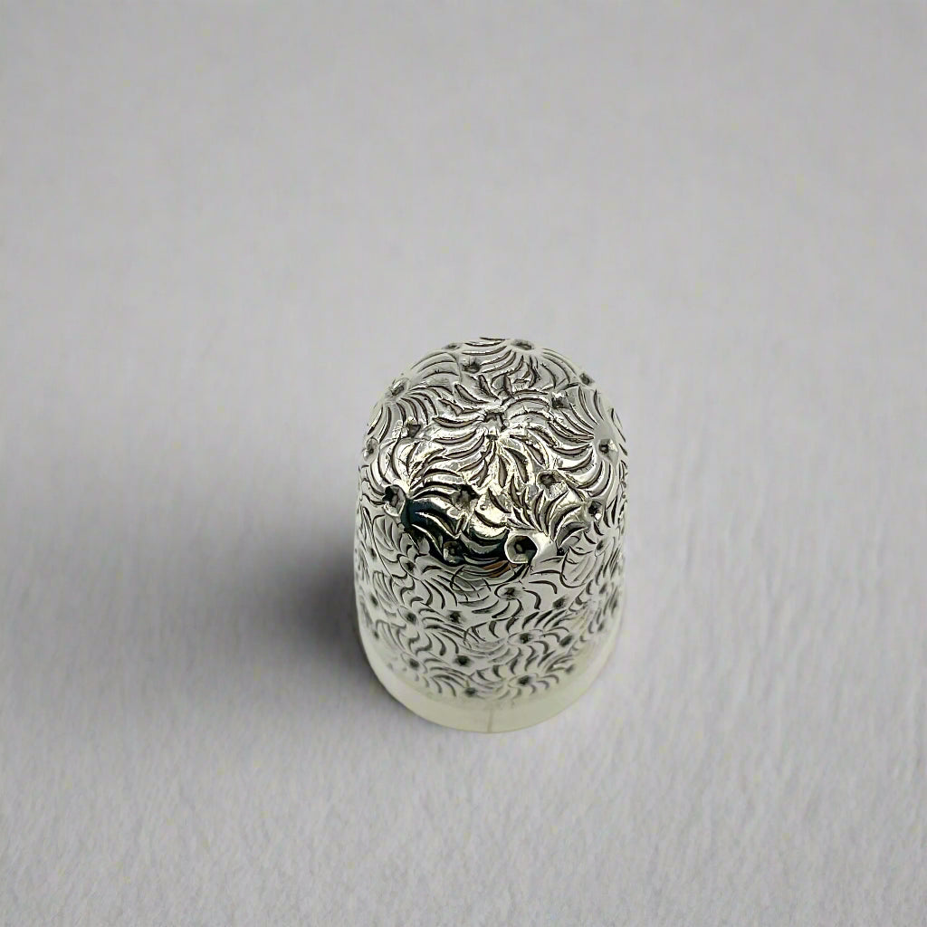Silver thimble with intricate patterns on a white material background