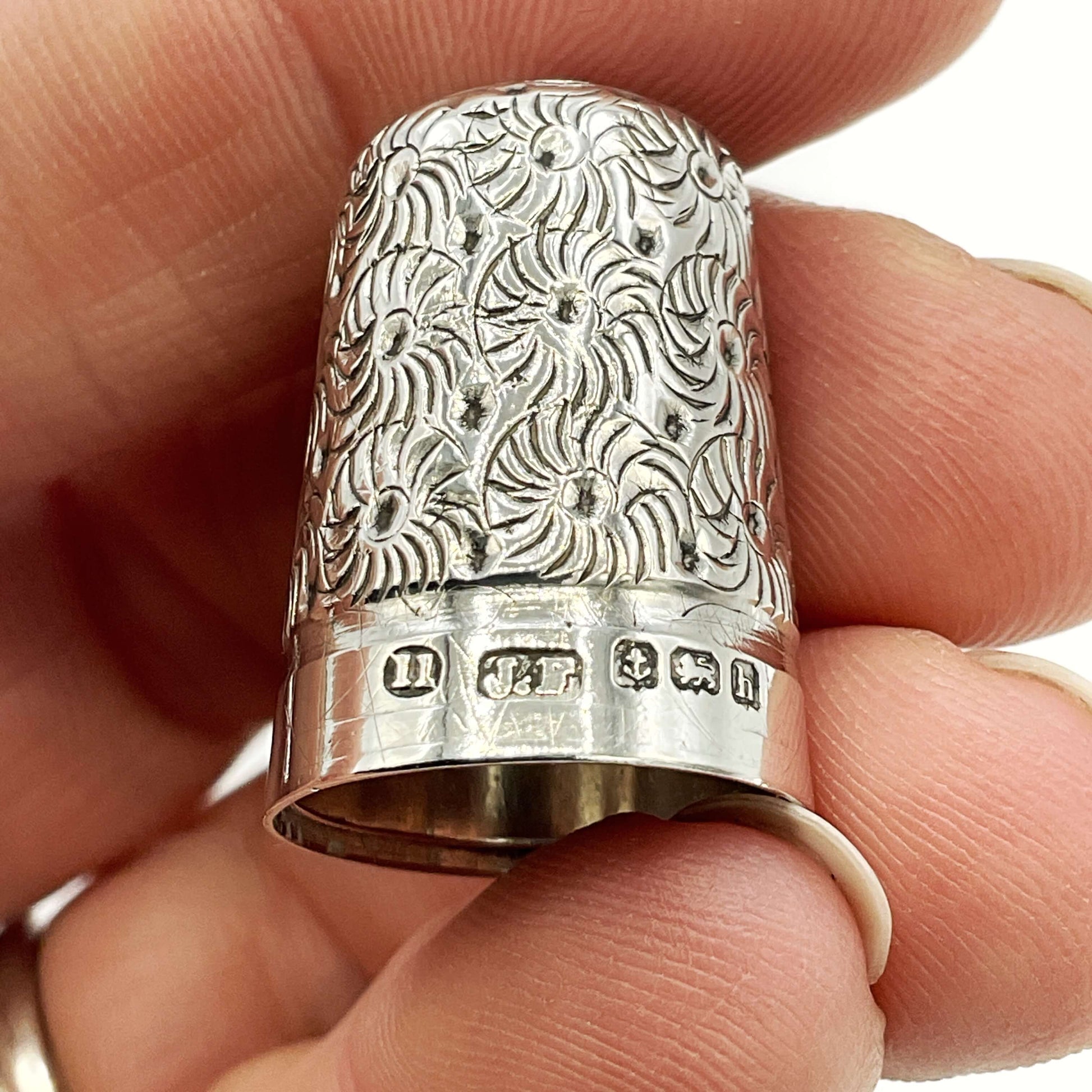 Silver thimble with intricate patterns held between fingers