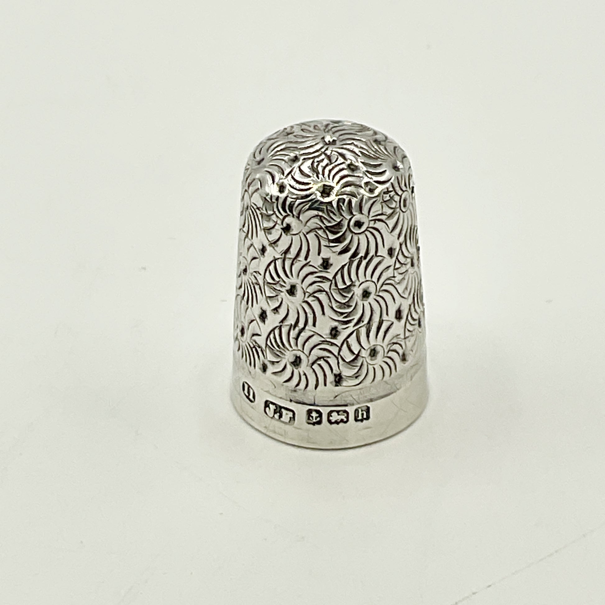 Silver thimble with intricate patterns on a white background showing hallmarks 