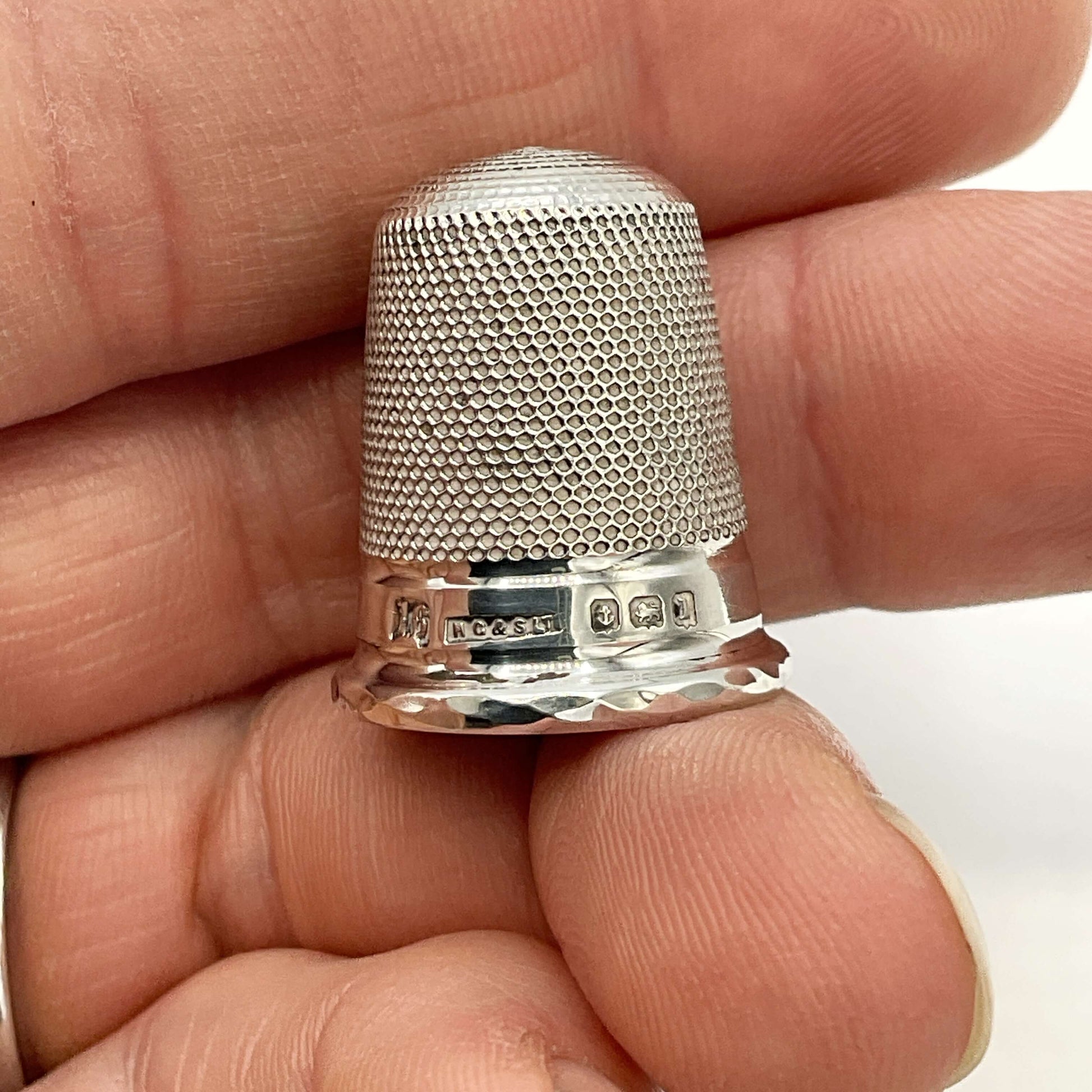 Silver thimble held between fingers against a neutral background