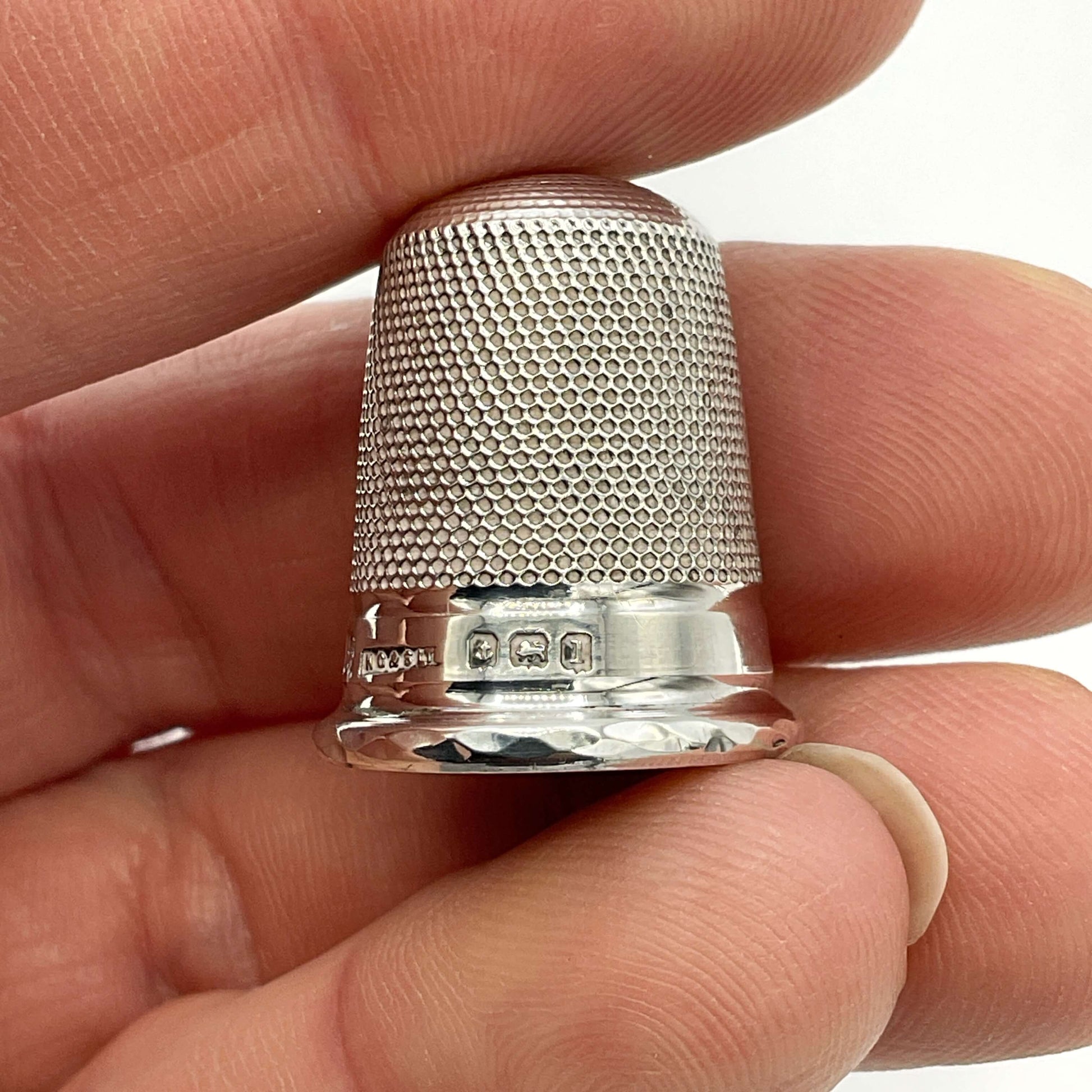 Silver thimble held between fingers against a neutral background showing the hallmarks 