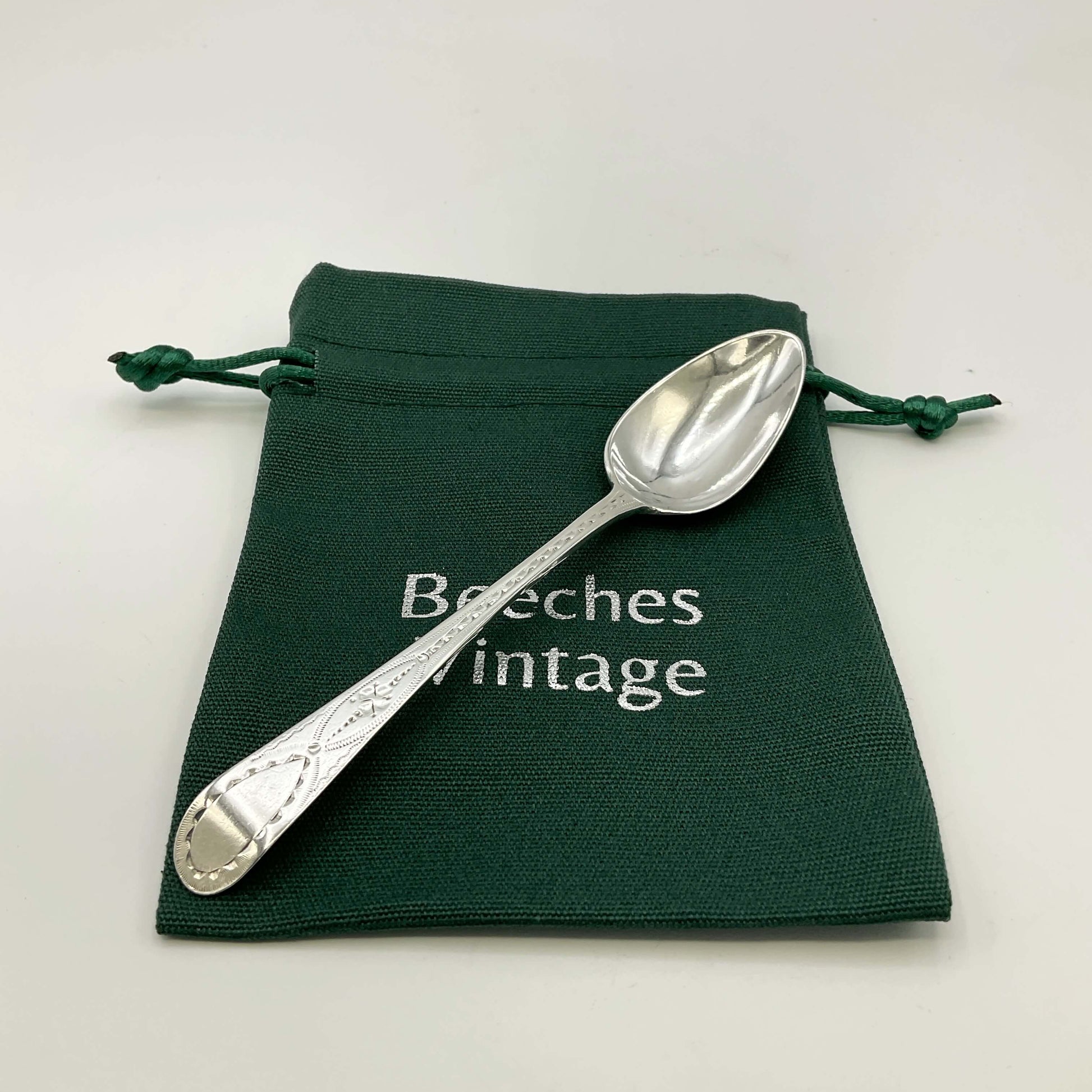 Silver spoon on a green drawstring bag with 'Beeches Vintage' text.