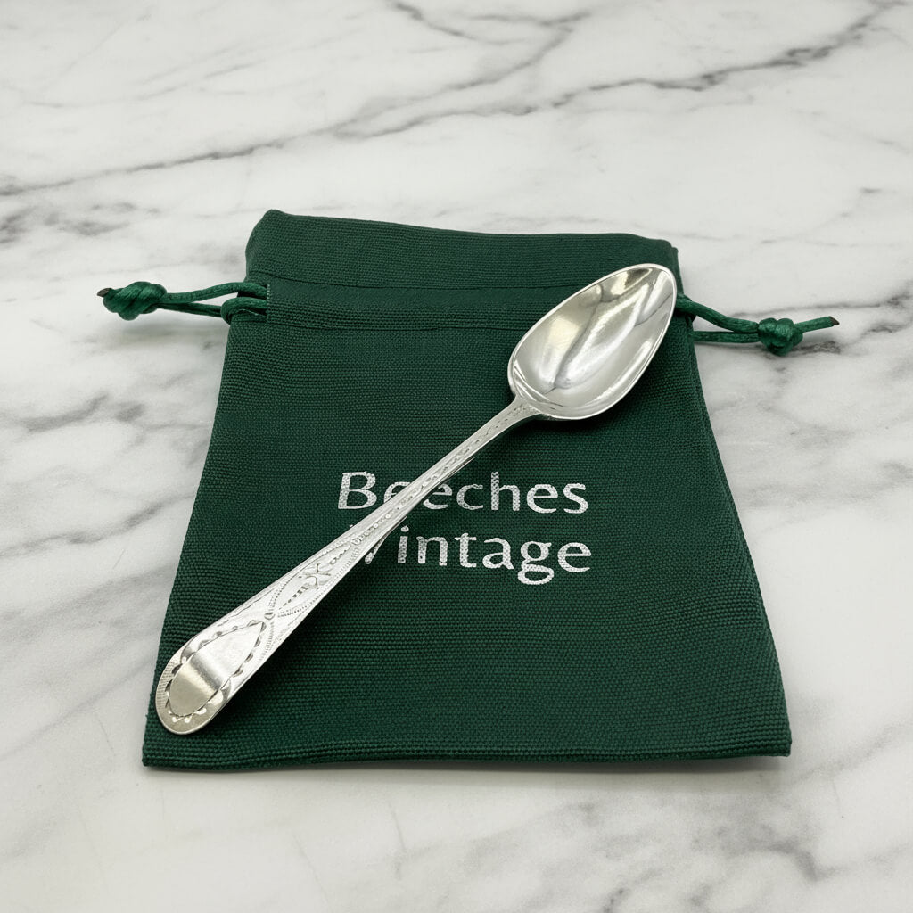 Silver spoon on a green drawstring bag with 'Beeches Vintage' text on a marble background
