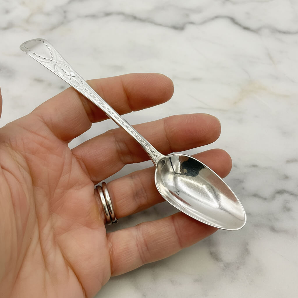 Silver spoon held in a hand against a marble background
