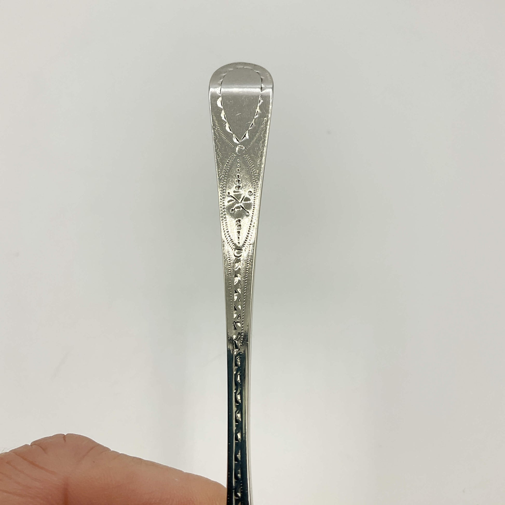 Silver spoon with intricate patterns held by a hand against a white background
