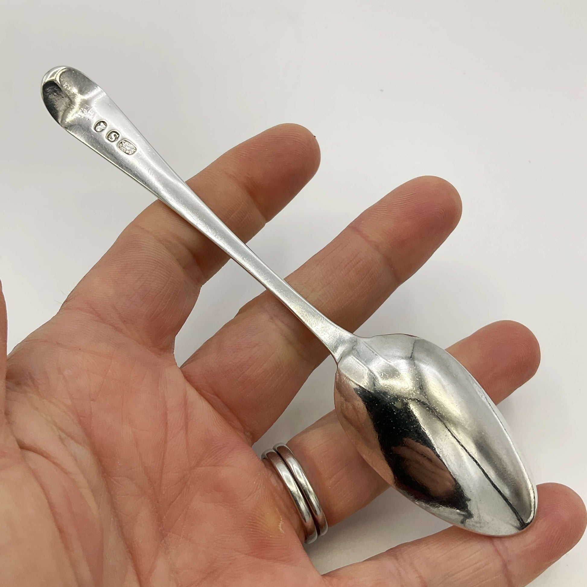 Silver spoon held in a hand against a white background