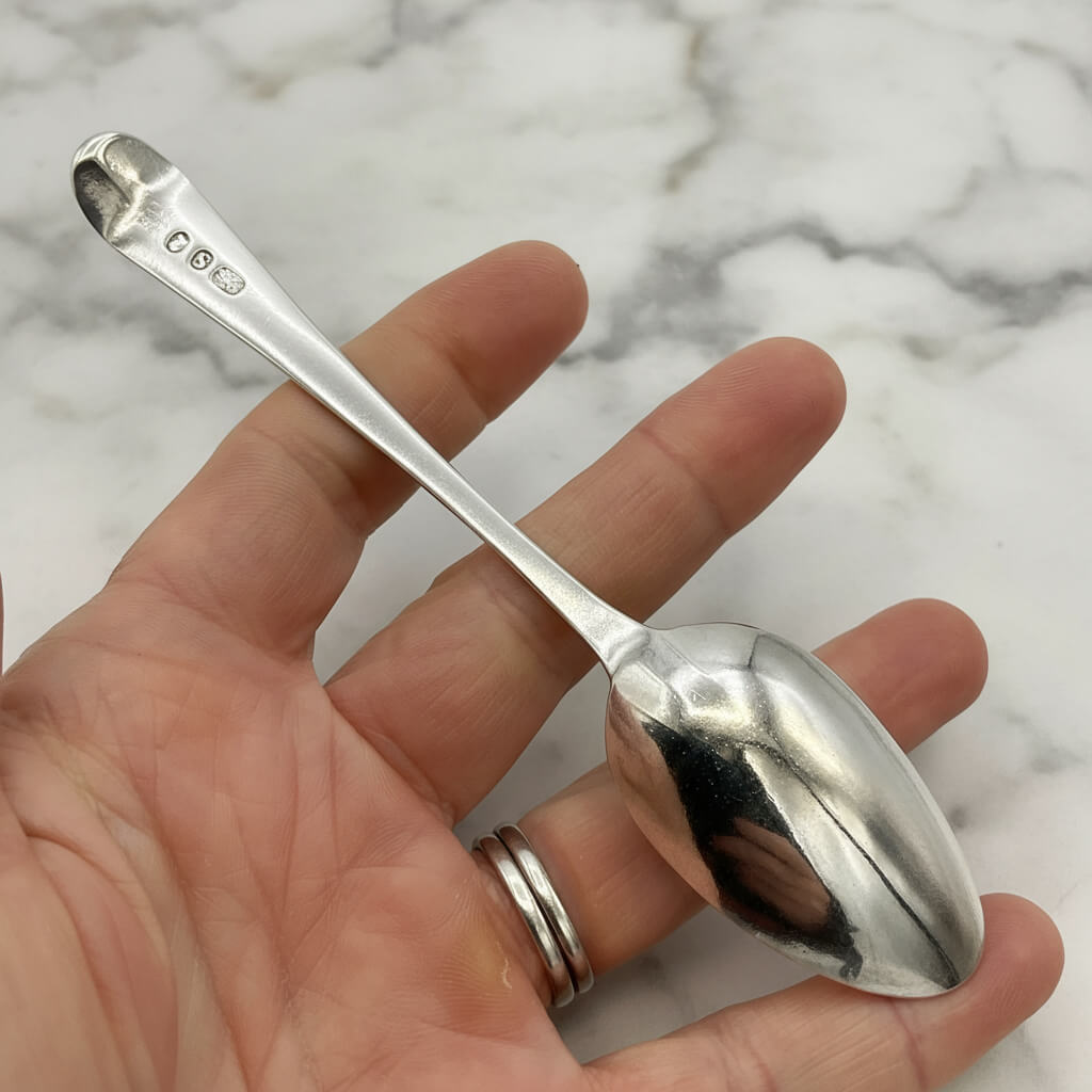 Silver spoon held in a hand against a marble background