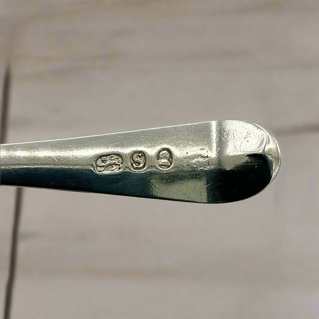 Close-up of a silver spoon with visible hallmarks on a wood background