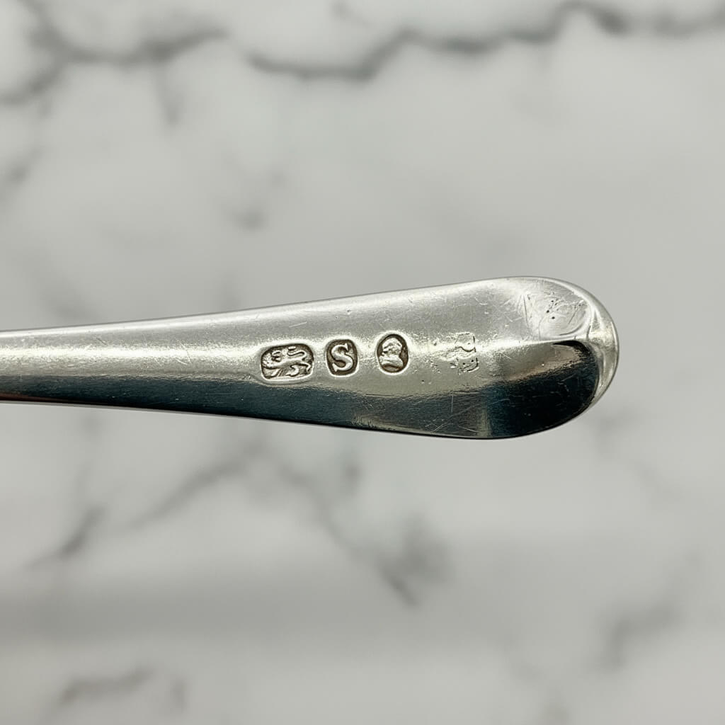 Close-up of a silver spoon with visible hallmarks on a marble background