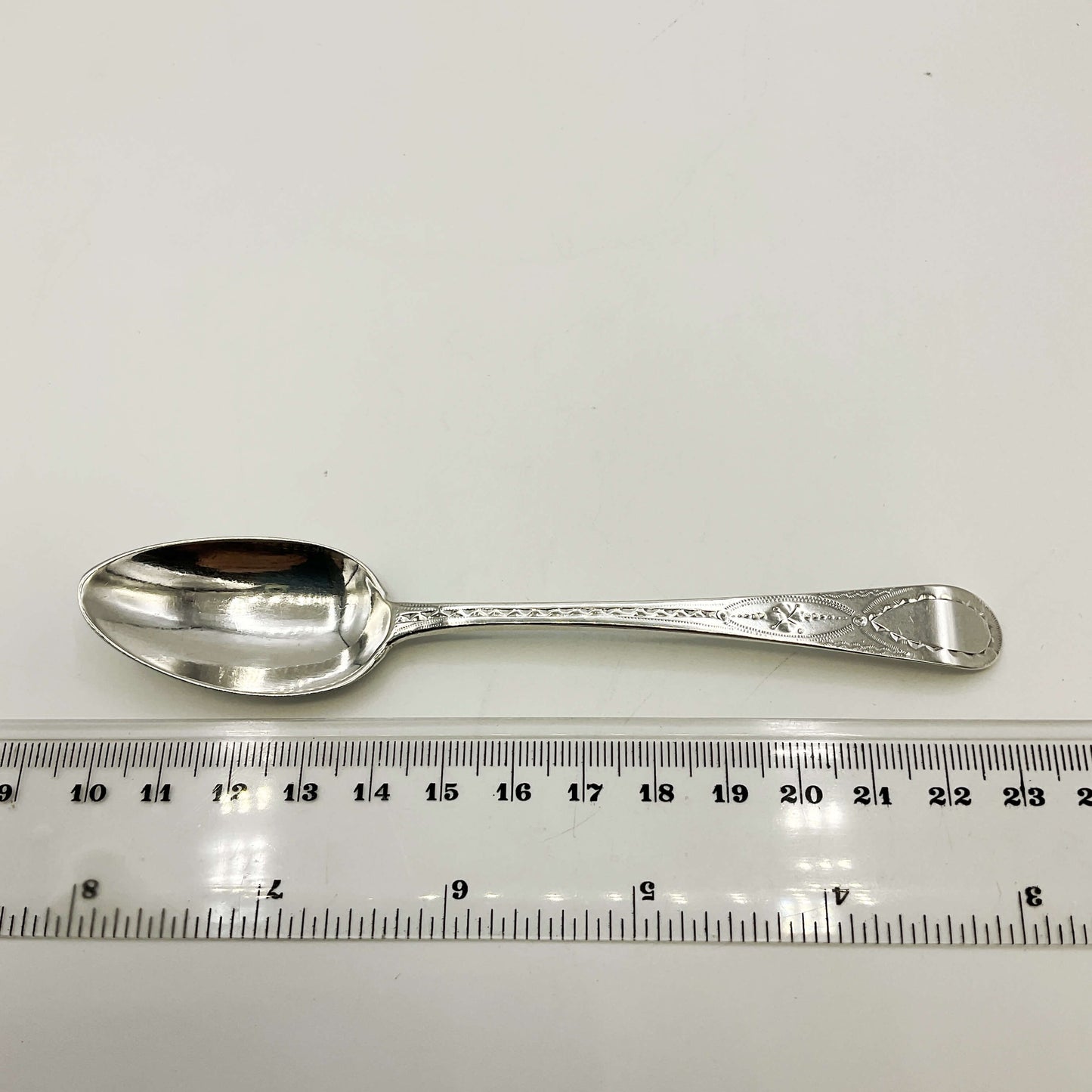 Silver spoon next to a ruler on a white background