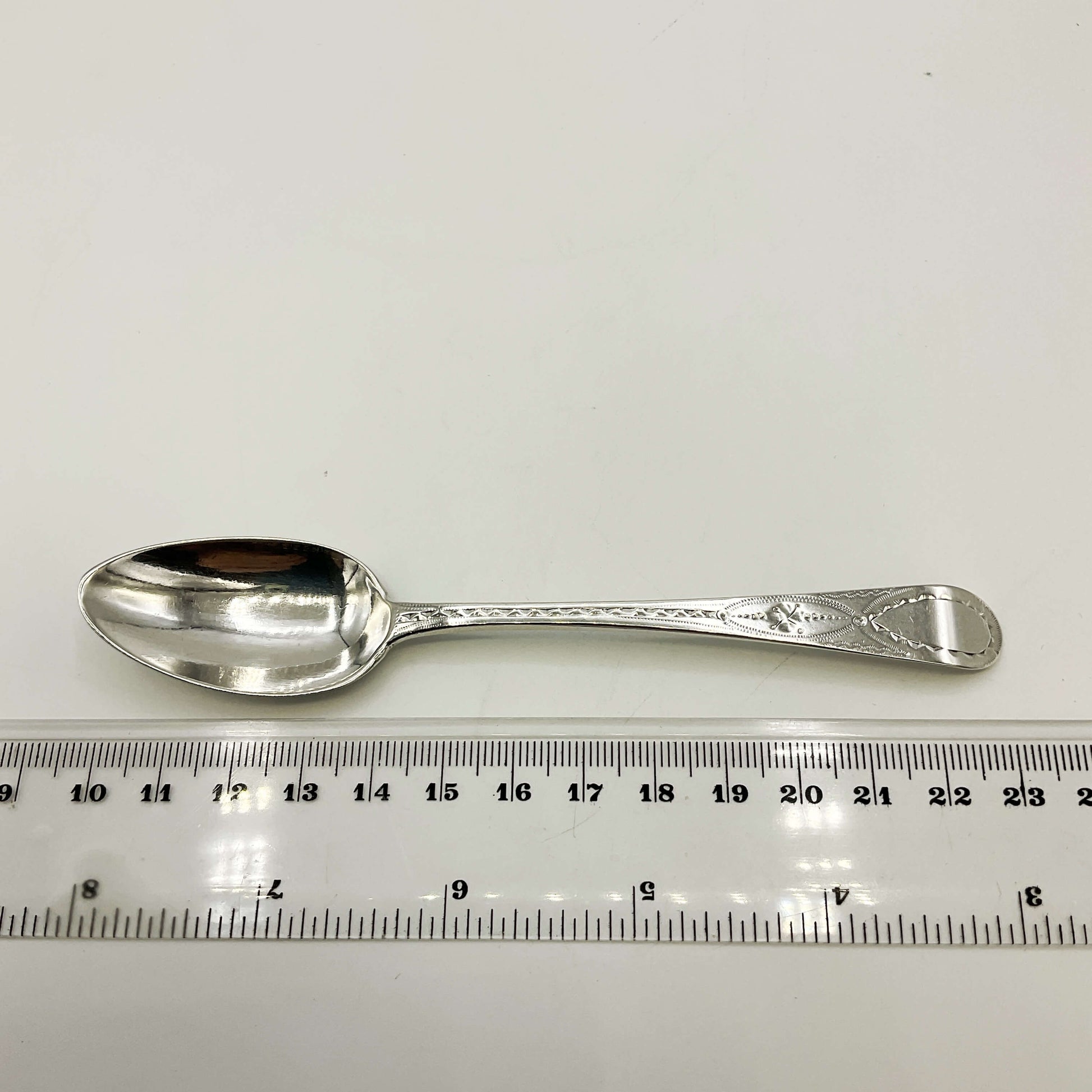 Silver spoon next to a ruler on a white background