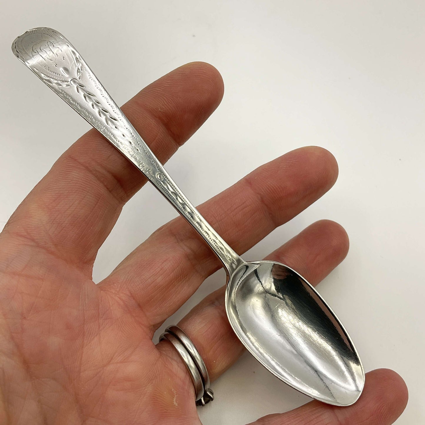 Silver spoon held in a hand against a white background