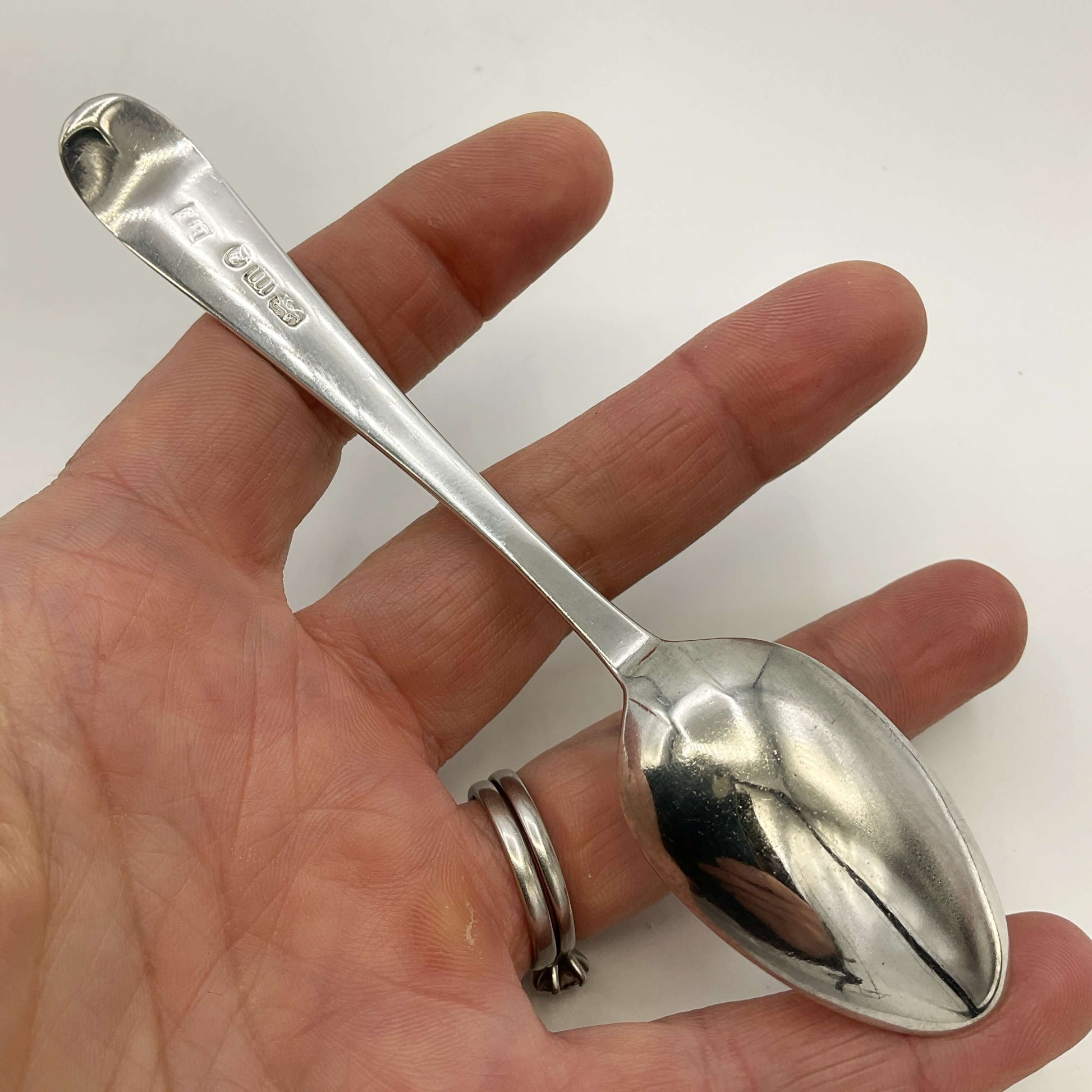 Back of Silver spoon held in a hand with a plain background